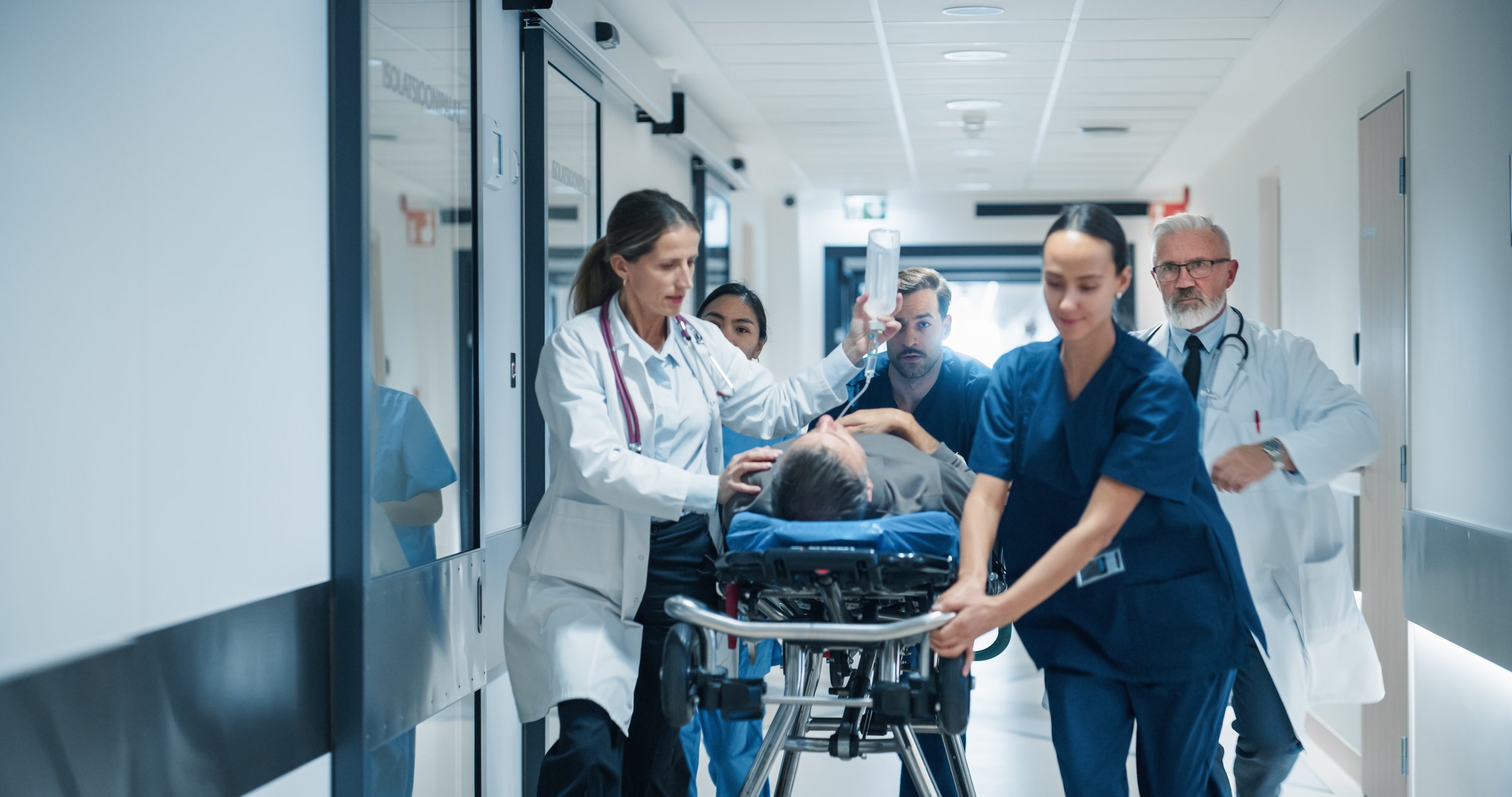 Diverse Emergency Medical Team Rushing Down a Hospital Corridor, Carefully Pushing a Stretcher with an Injured Patient. Nurses and Doctors Coordinate Urgent Life-Saving Efforts