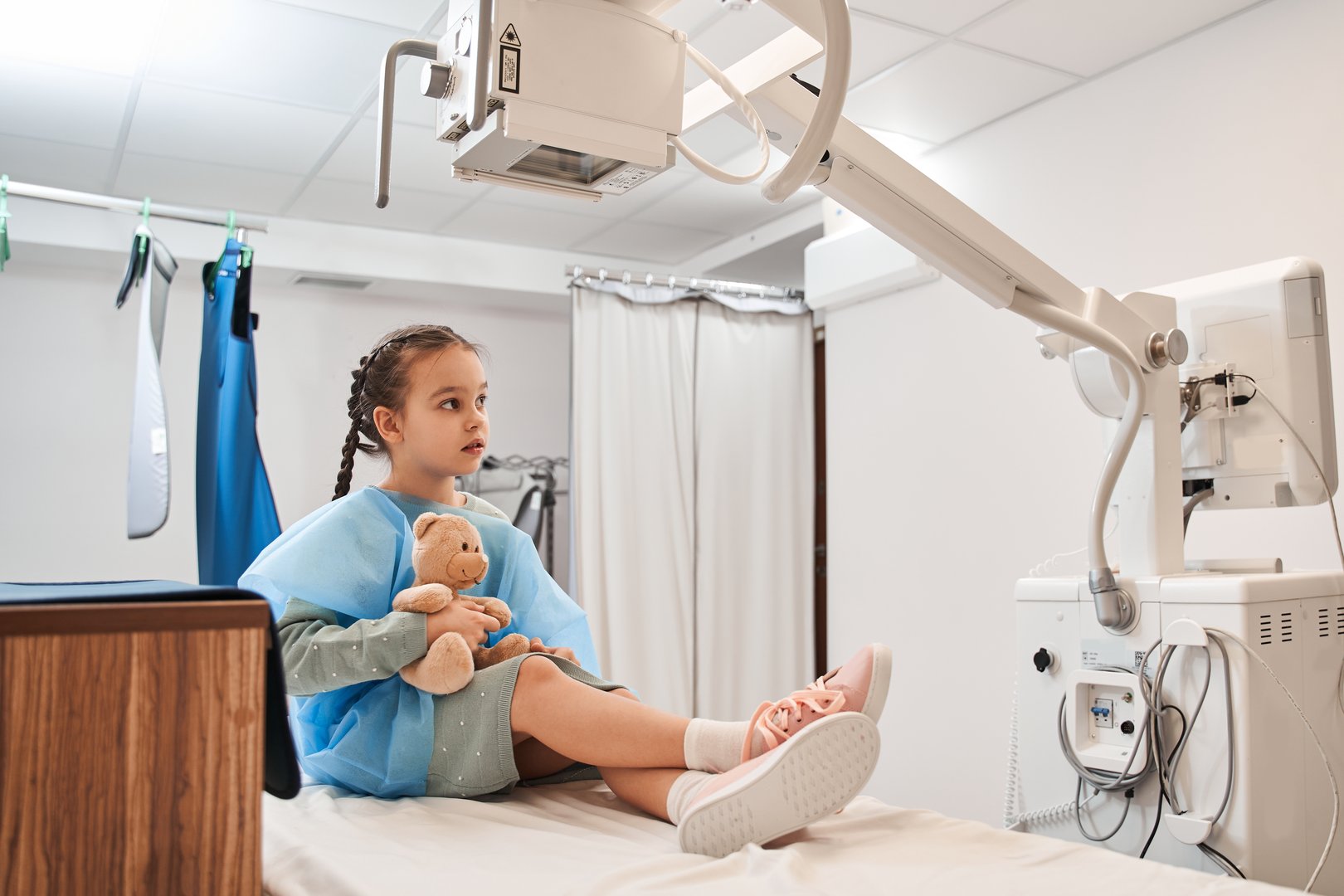 Im scary. Little female child sitting at the hospital bed and embracing her teddy bear while waiting for the procedure. Stock photo