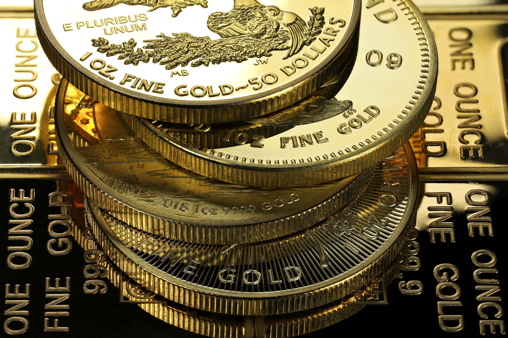 4 different 1 ounce gold bullion coins on a layer of gold ingots