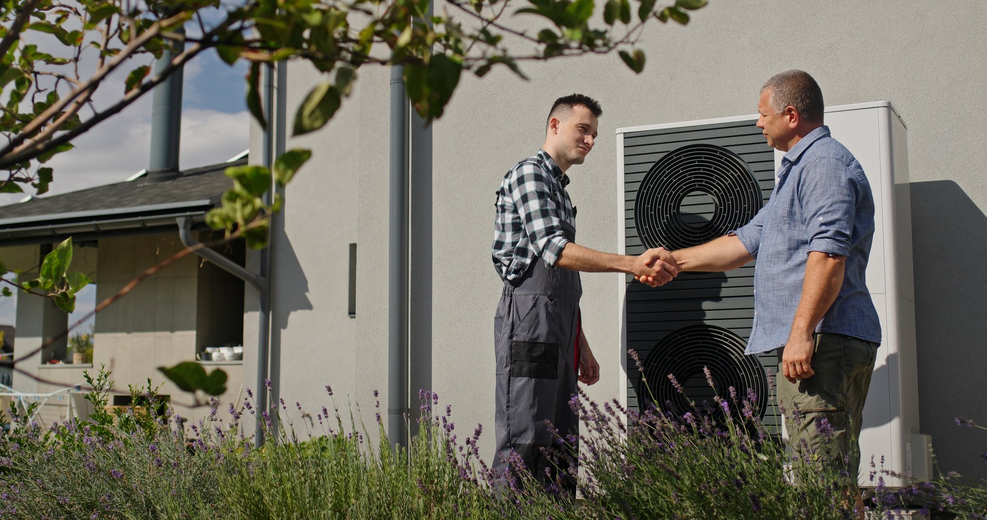 A technician and a homeowner are shaking hands beside an external heat pump unit, signaling a successful consultation or installation.