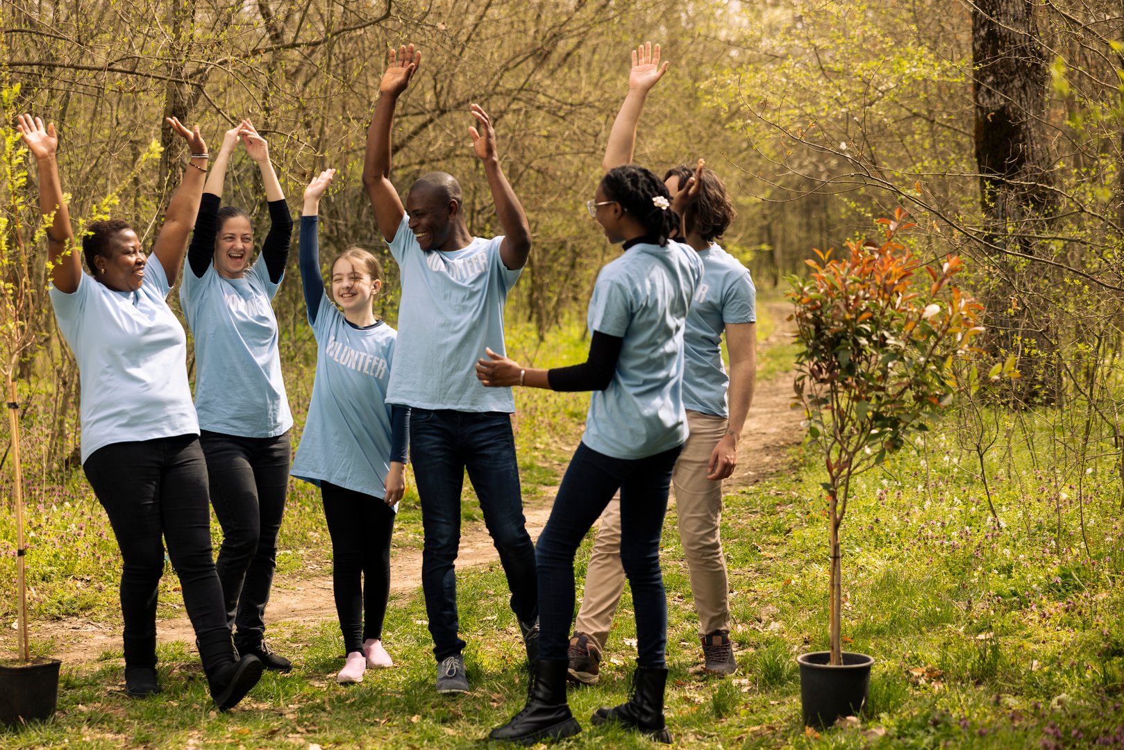 Team of diverse environmentalists linking hands to celebrate a successful mission of preserving natural habitat, saving the ecosystem. Group of people collaborate to grow more trees in the forest.