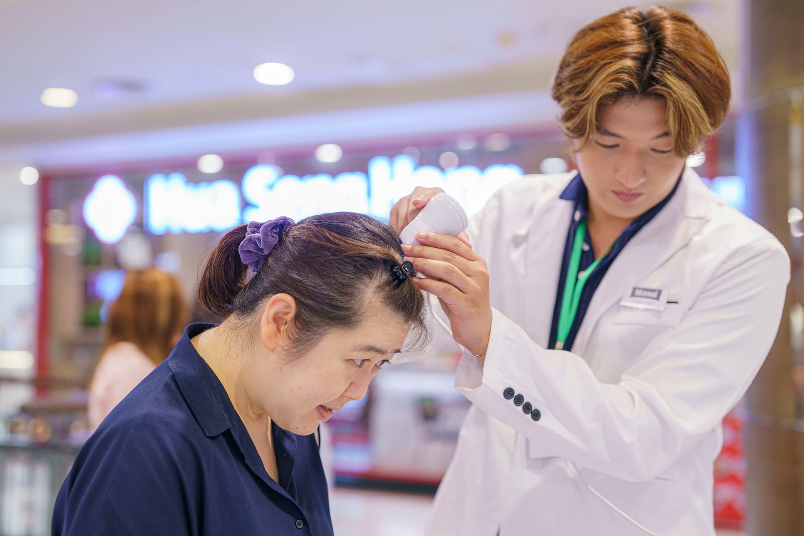 A healthcare professional examines a womans scalp with a device inside a clinic.