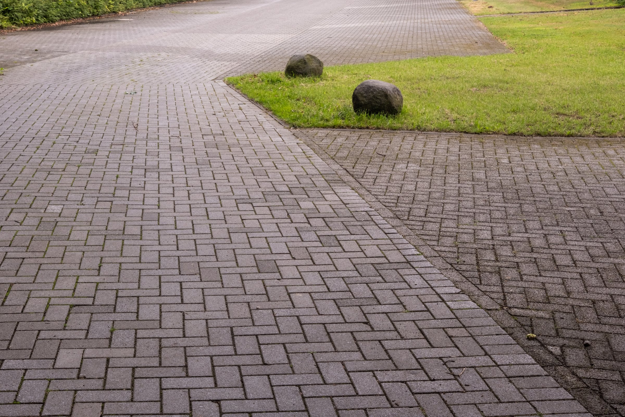 Pathway and parking area made of gray interlocking pavers with grass and rocks