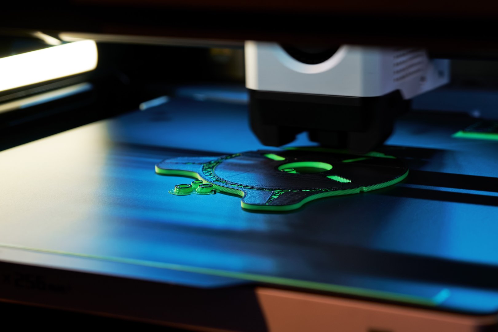 A 3D printer operates efficiently, layering vibrant green filament to form an intricate object. The workspace is illuminated by soft overhead light, highlighting the technology.