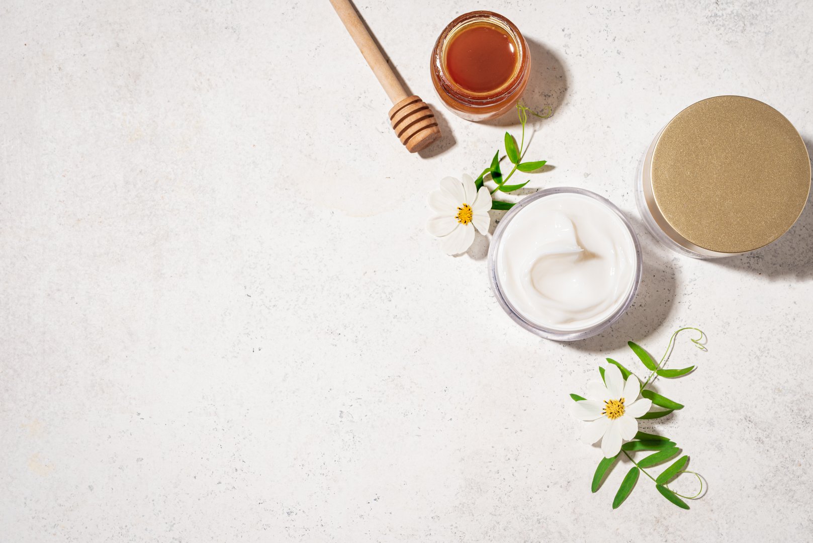 Cosmetic rich cream with natural honey. Jar of nourishing beauty cream products, honey and white flowers on white background, top view, copy space.