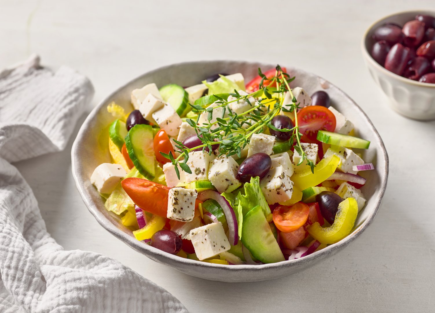 bowl of healthy fresh greek salad on white kitchen table
