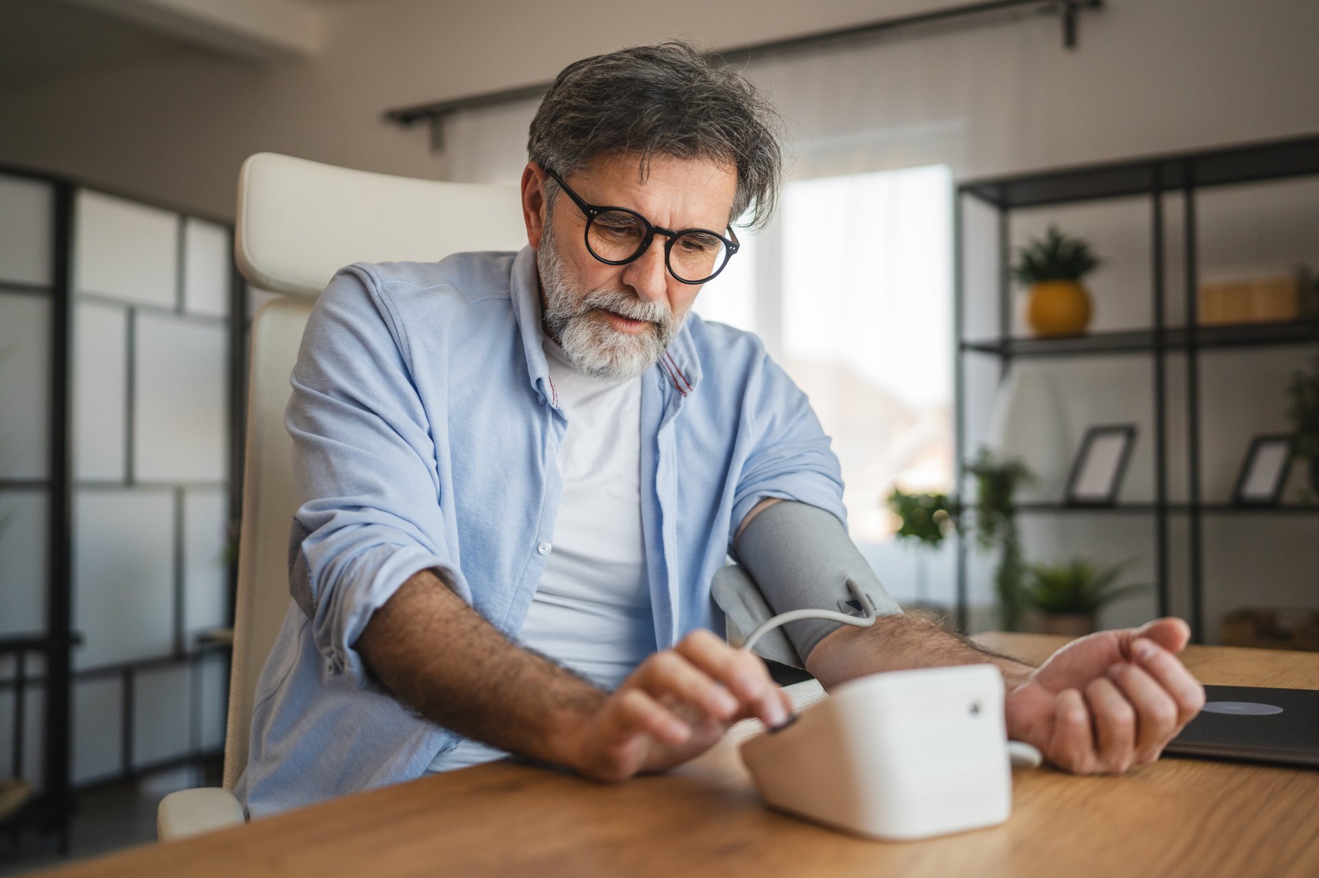 worried mature man use blood pressure device on hand to check health results while sit at home