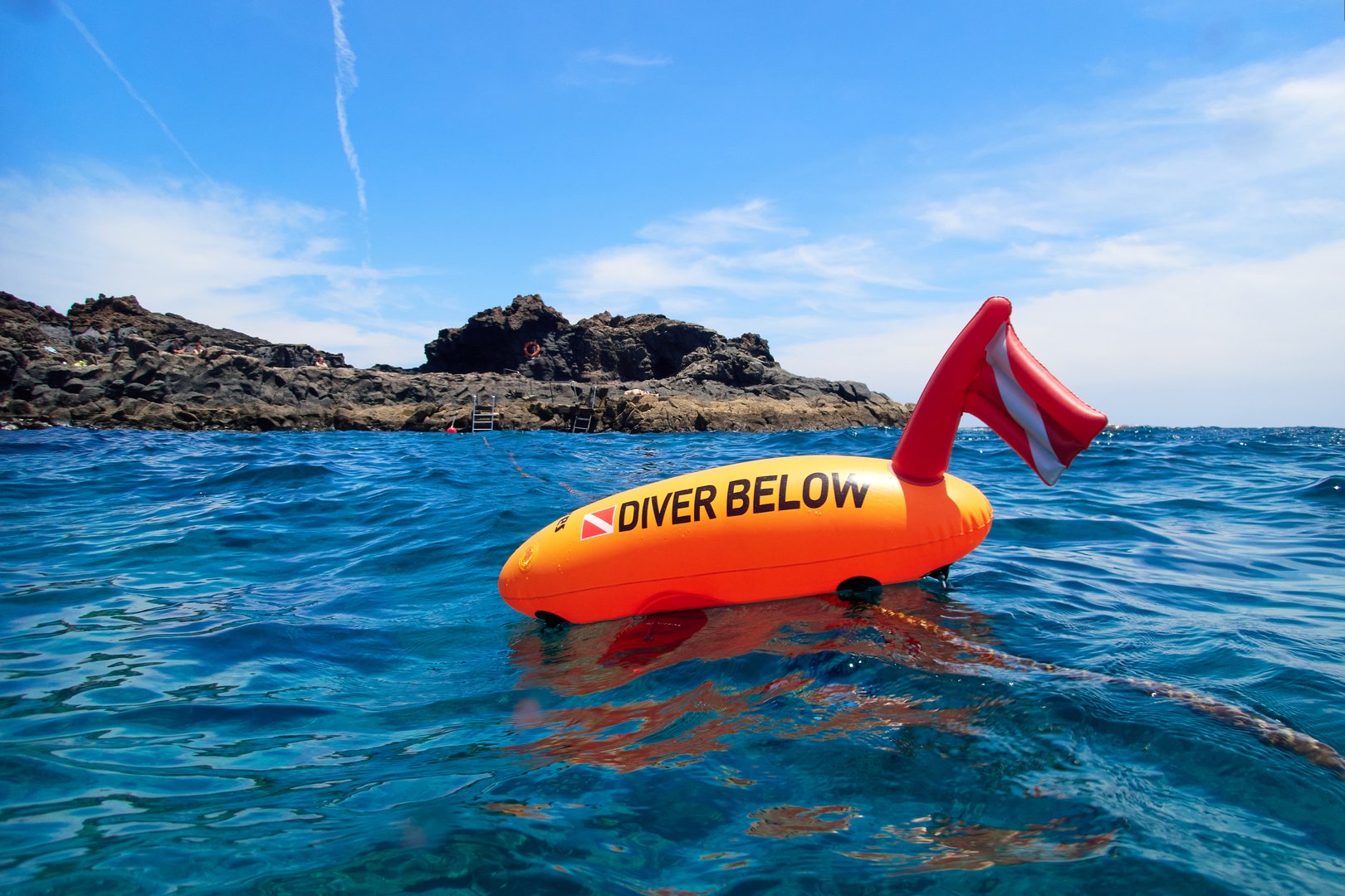 An orange diving buoy with text &quot;Diver below&quot; floats on the surface of the blue Atlantic Ocean. Safety equipment for divers.