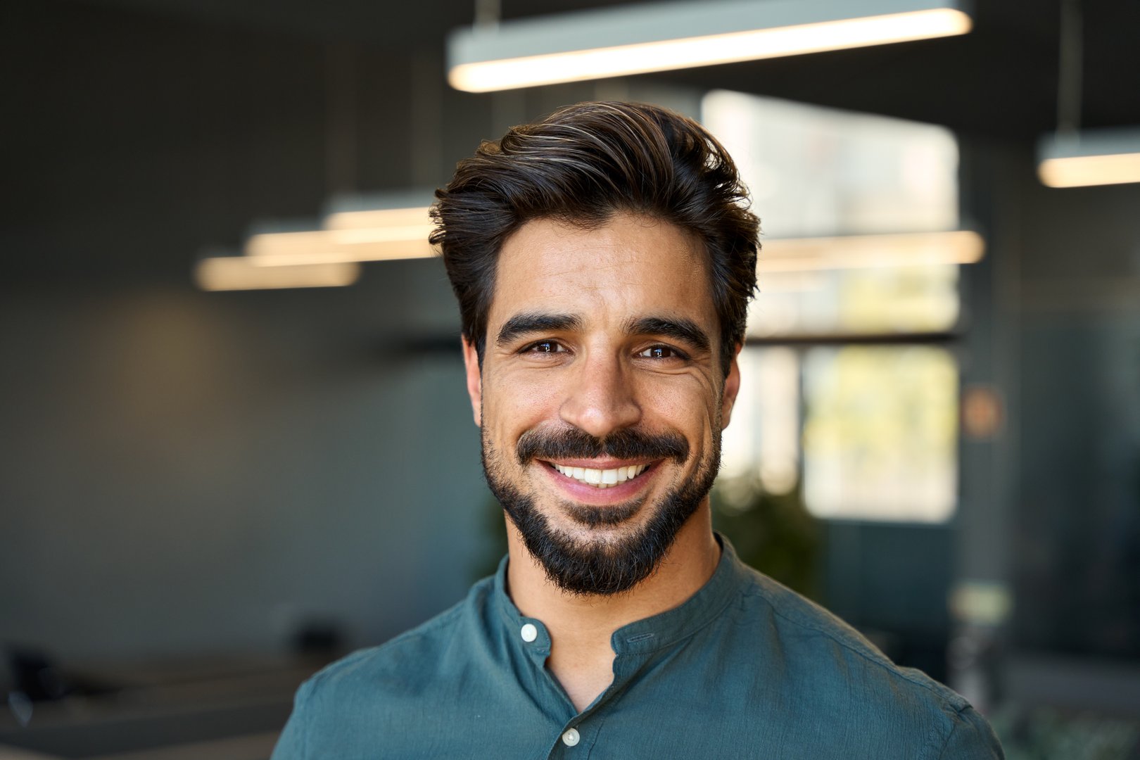Smiling handsome young business man looking at camera in office, headshot close up corporate portrait. Happy Latin businessman, male entrepreneur, professional manager or company employee at work.