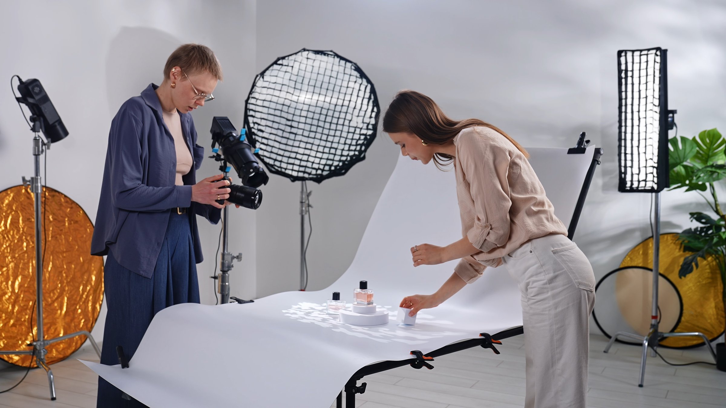 Backstage. A photographer and assistant arrange products for a perfume photo shoot in a studio with professional lighting.