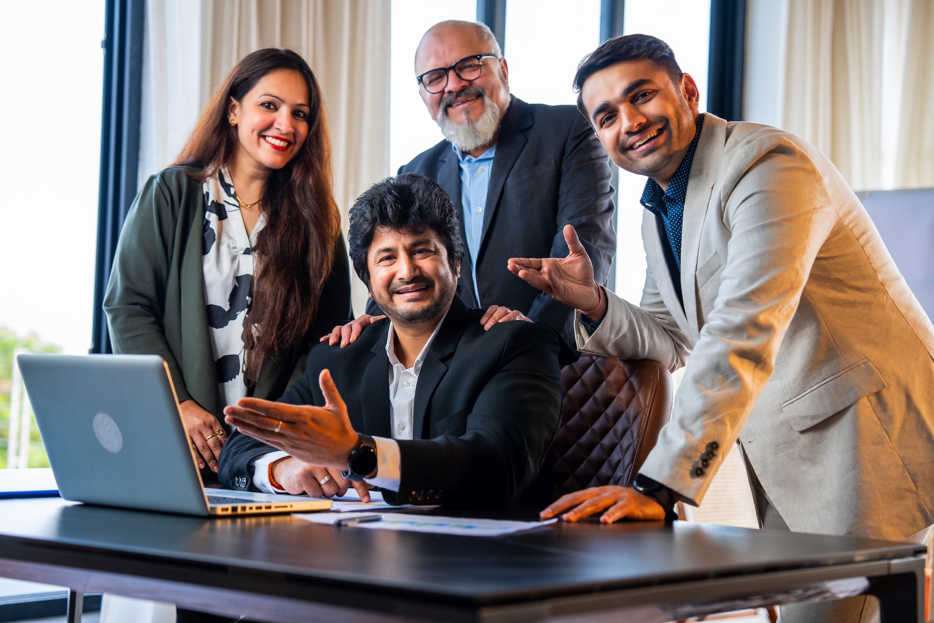 Indian Asian group of successful corporate professionals in formal attire working on laptop, reviewing business documents or reports, and discussing serious matters in an office setting