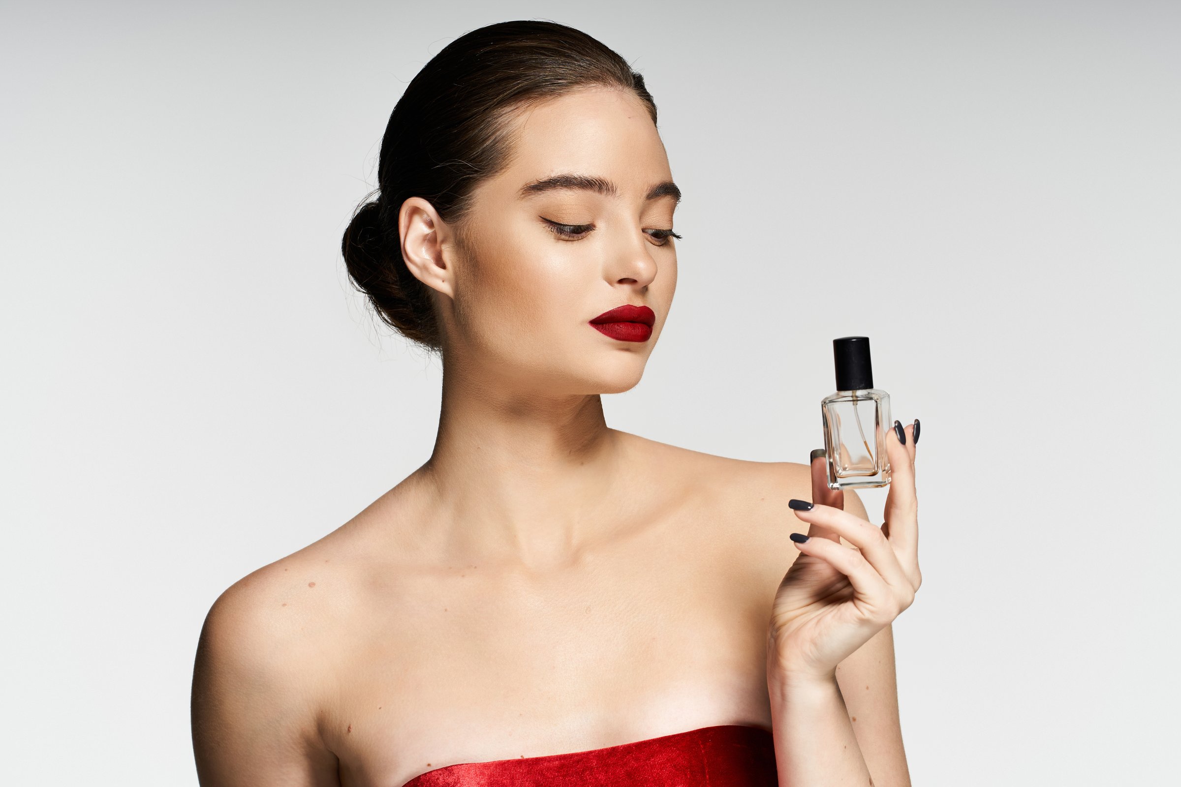 A young woman confidently poses in the studio, elegantly holding a perfume bottle.