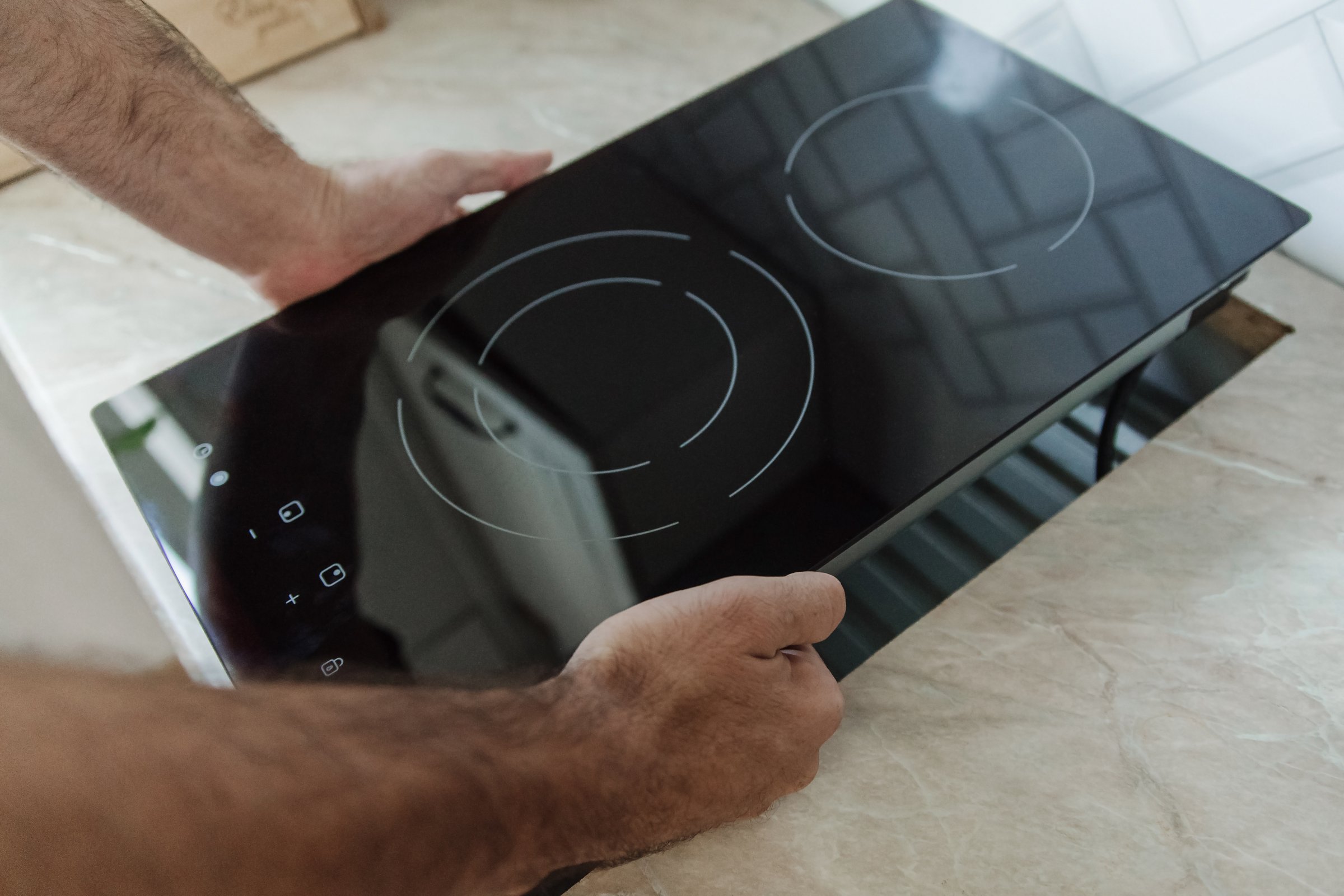 A man installs a black glass-ceramic hob cooktop on a kitchen countertop