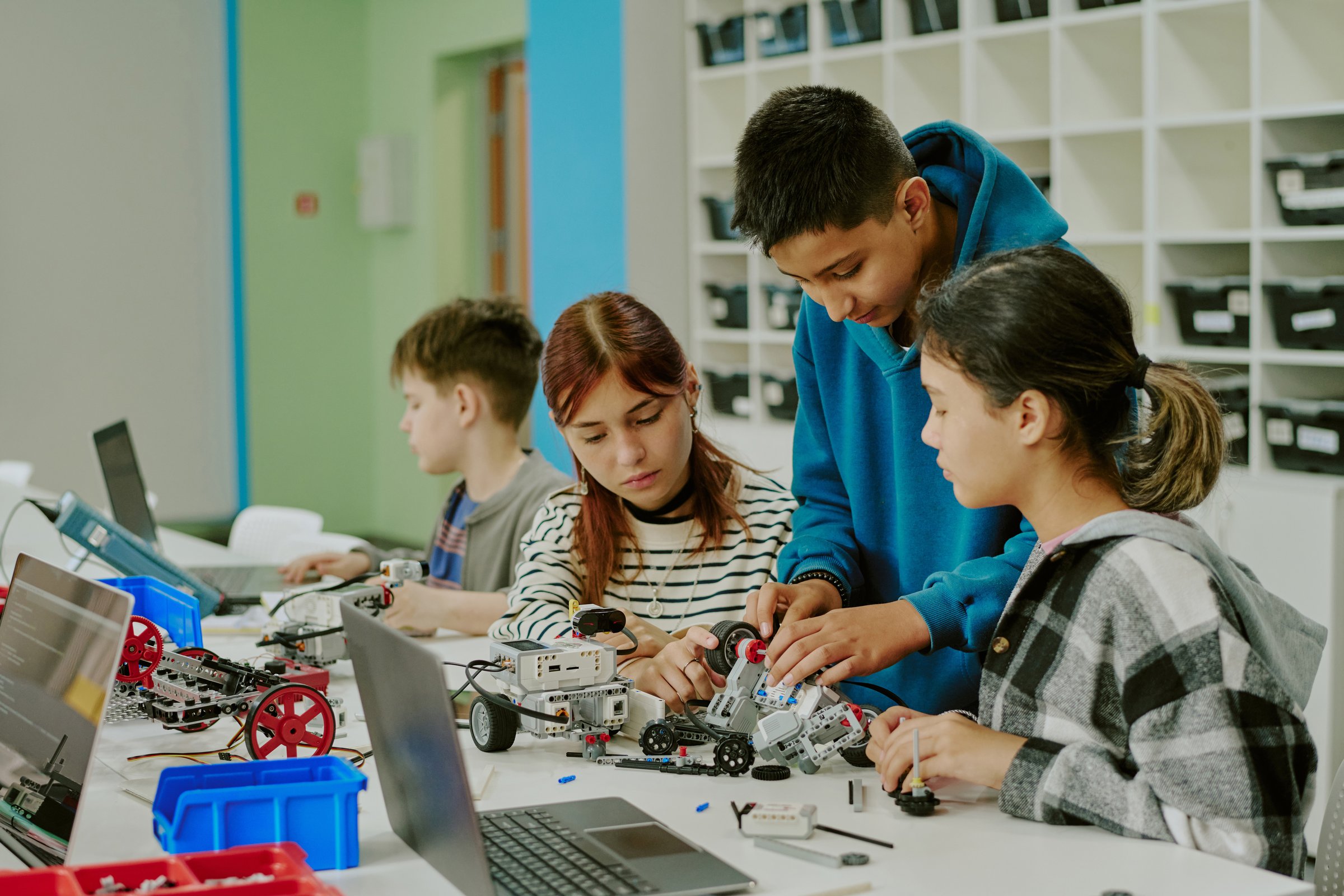 Group of students busy with making prototype of robot while their classmate trying to write code in background