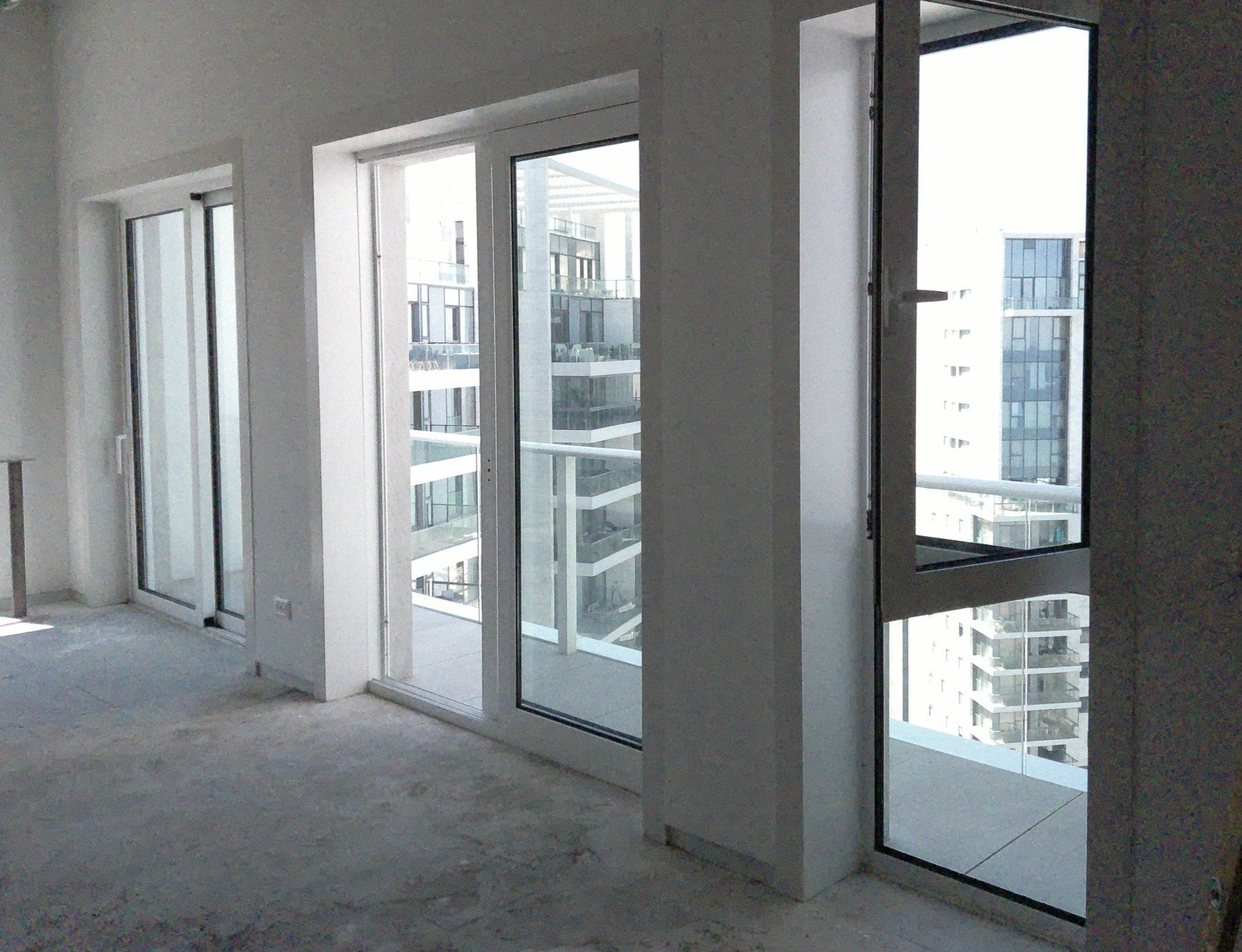 Unfurnished room with large glass doors and windows, opening to a balcony with a view of modern apartment buildings.