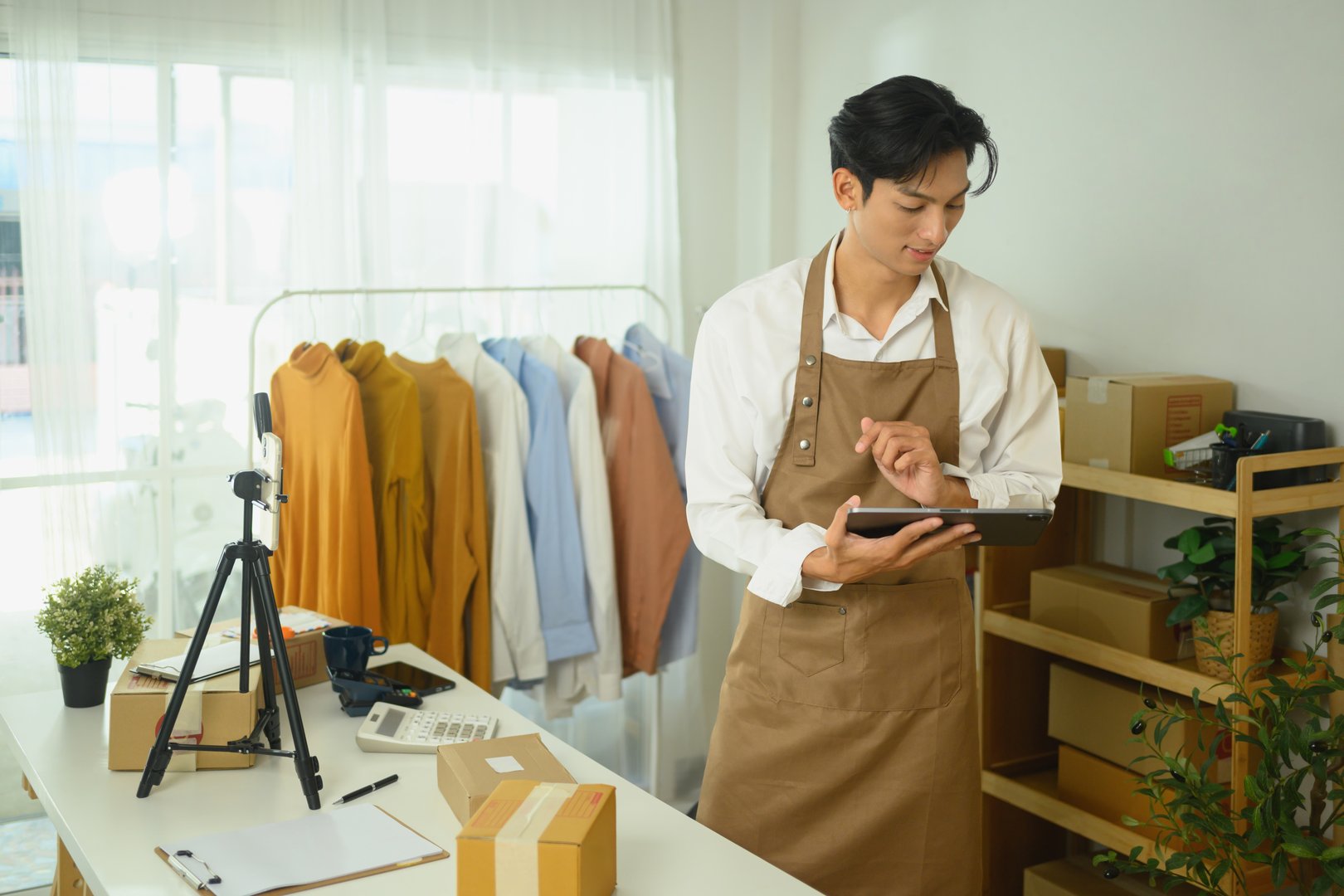An online store owner checking orders on digital tablet while standing in a workspace.
