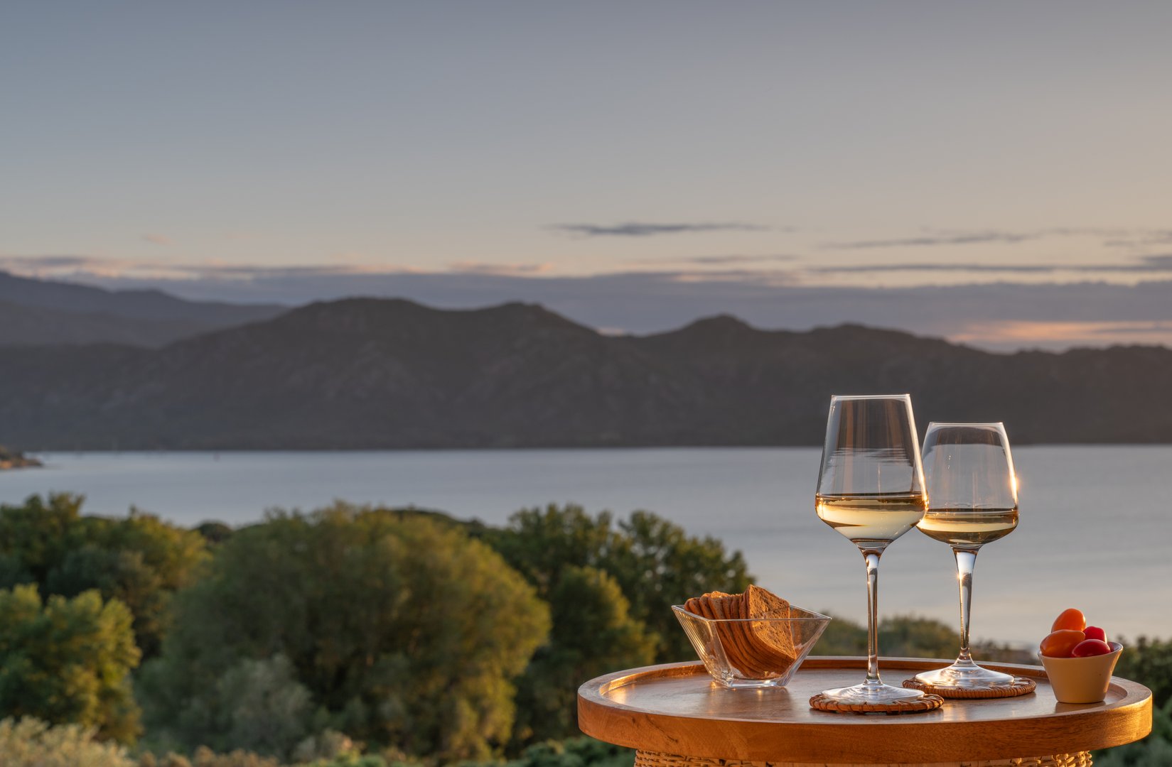A wooden table with snacks and two wineglasses glasses against a beautiful scenic backdrop