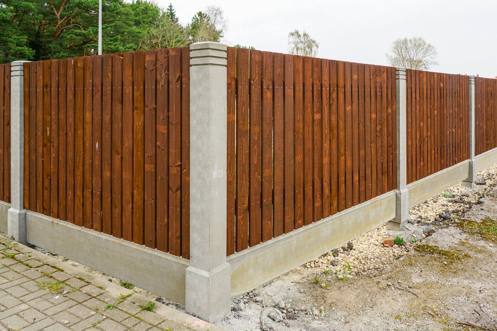New fence with factory-made concrete posts and foundations and brown wooden plank spans, prefabricated construction, wooden fence panels
