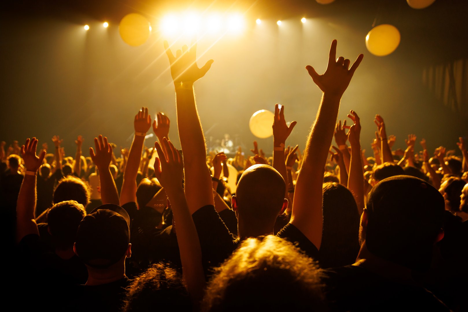 A cheering audience lifts hands toward the stage during a live concert bathed in golden light. The image reflects joy, unity, and shared energy of live performance moments. Ideal for event and entertainment themes.
