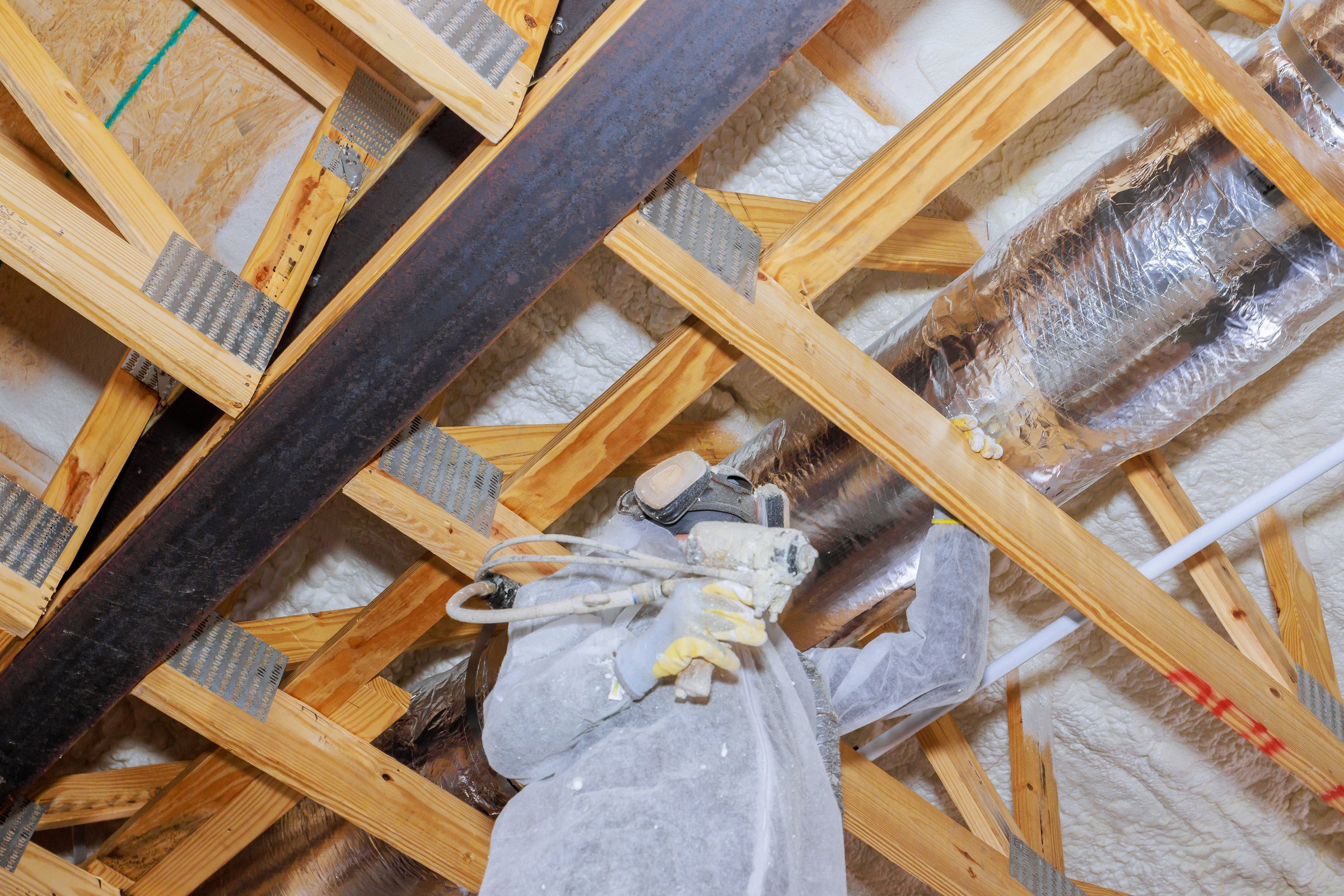 Construction worker is installing thermal barrier insulation in an attic with spray equipment to improve energy efficiency.