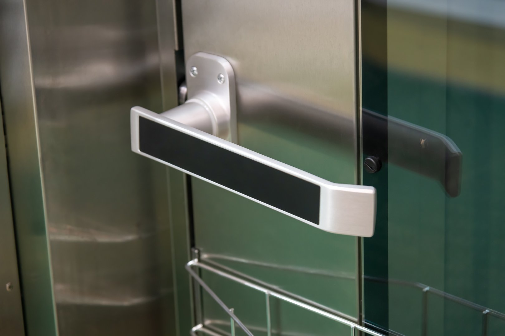 A stainless steel door handle attached to a glass door enhances the modern look of an urban building. Sunlight reflects off the surface, highlighting contemporary design elements.
