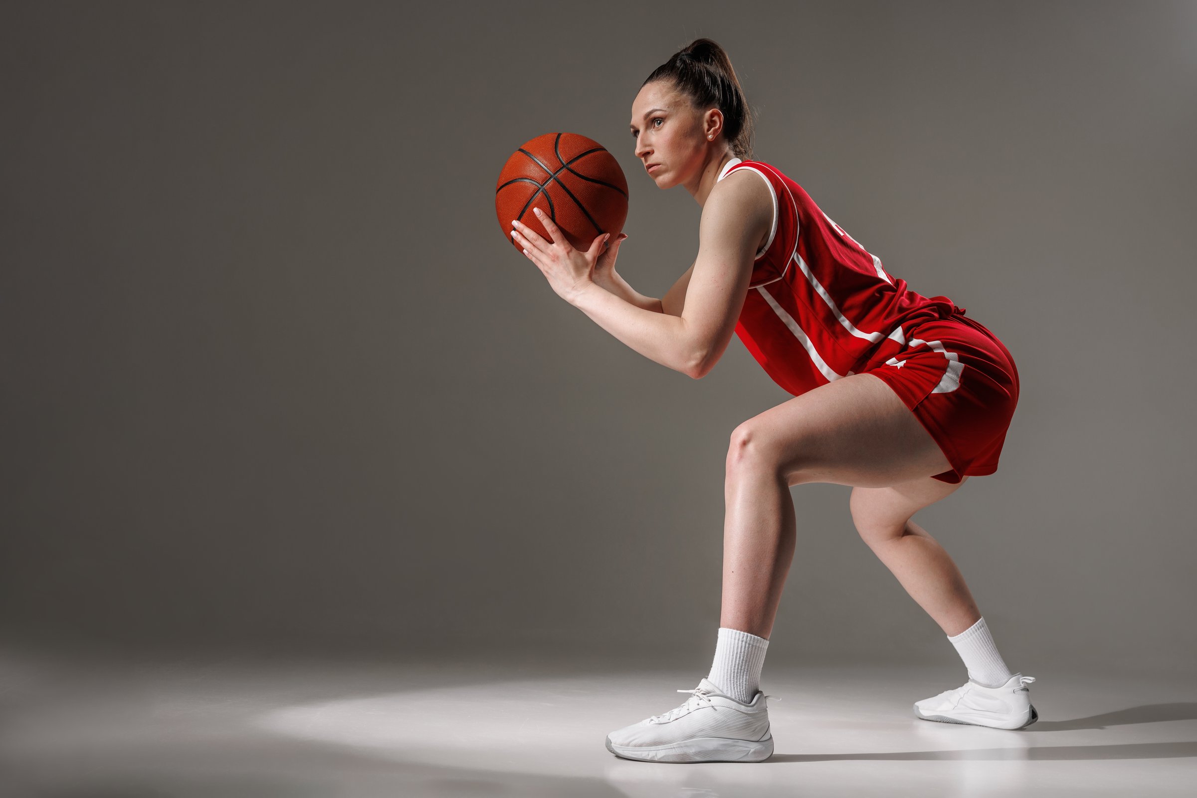 Confident womenâs basketball athlete in red uniform poised to pass, demonstrating strength and focus in the game studio