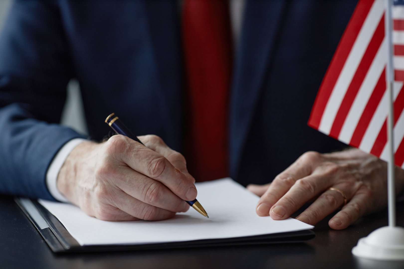 Close up on hands of Caucasian middle aged male official signing document at desk with American flag at political office