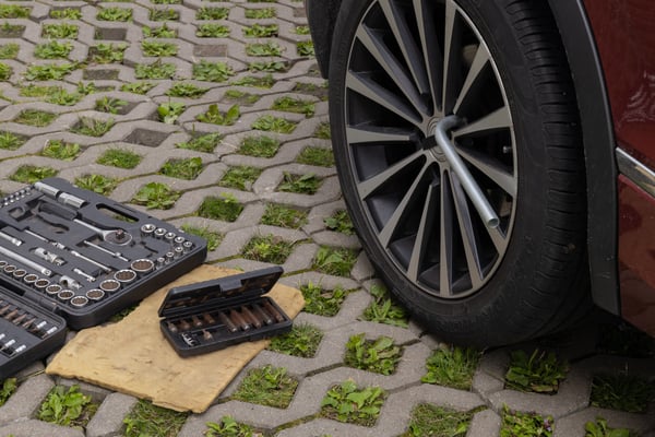 car wheel with wrench attached and toolboxes lying nearby on green block pavement car maintenance setup