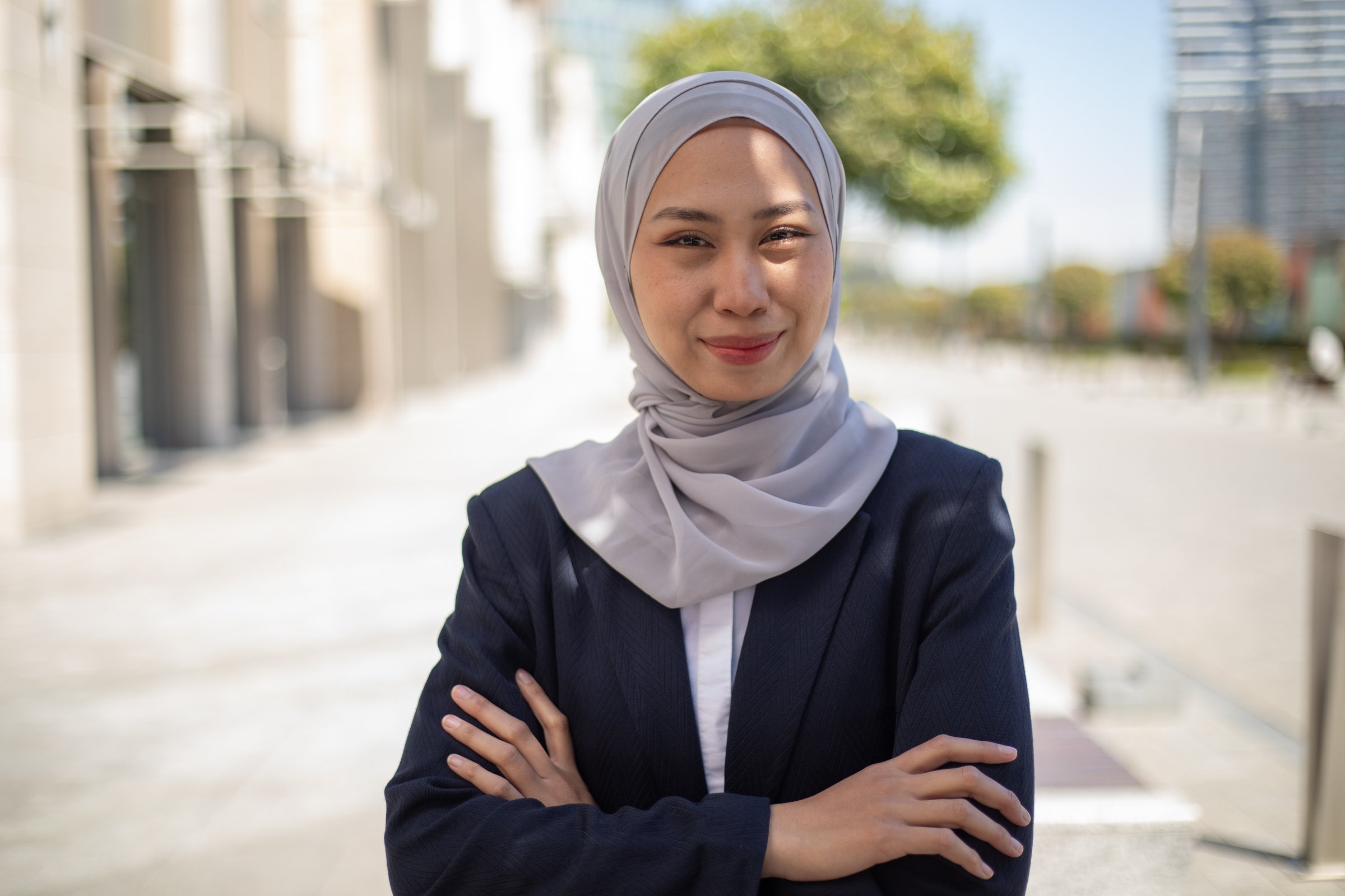 Portrait of smiling businesswoman wearing hijab standing with arms crossed in the city