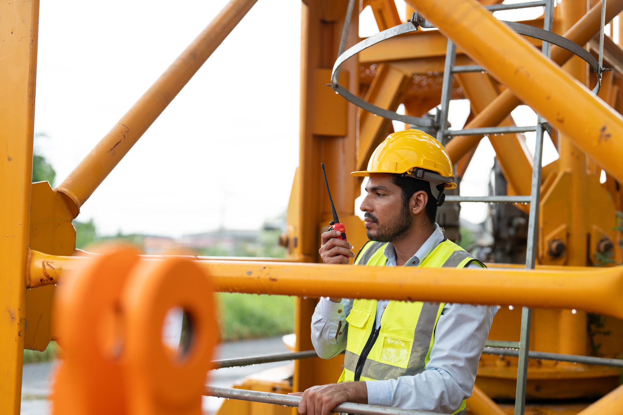 Asian male engineer wearing safety vests and helmet climbing metal ladder inspection and maintenance tower crane at construction site.