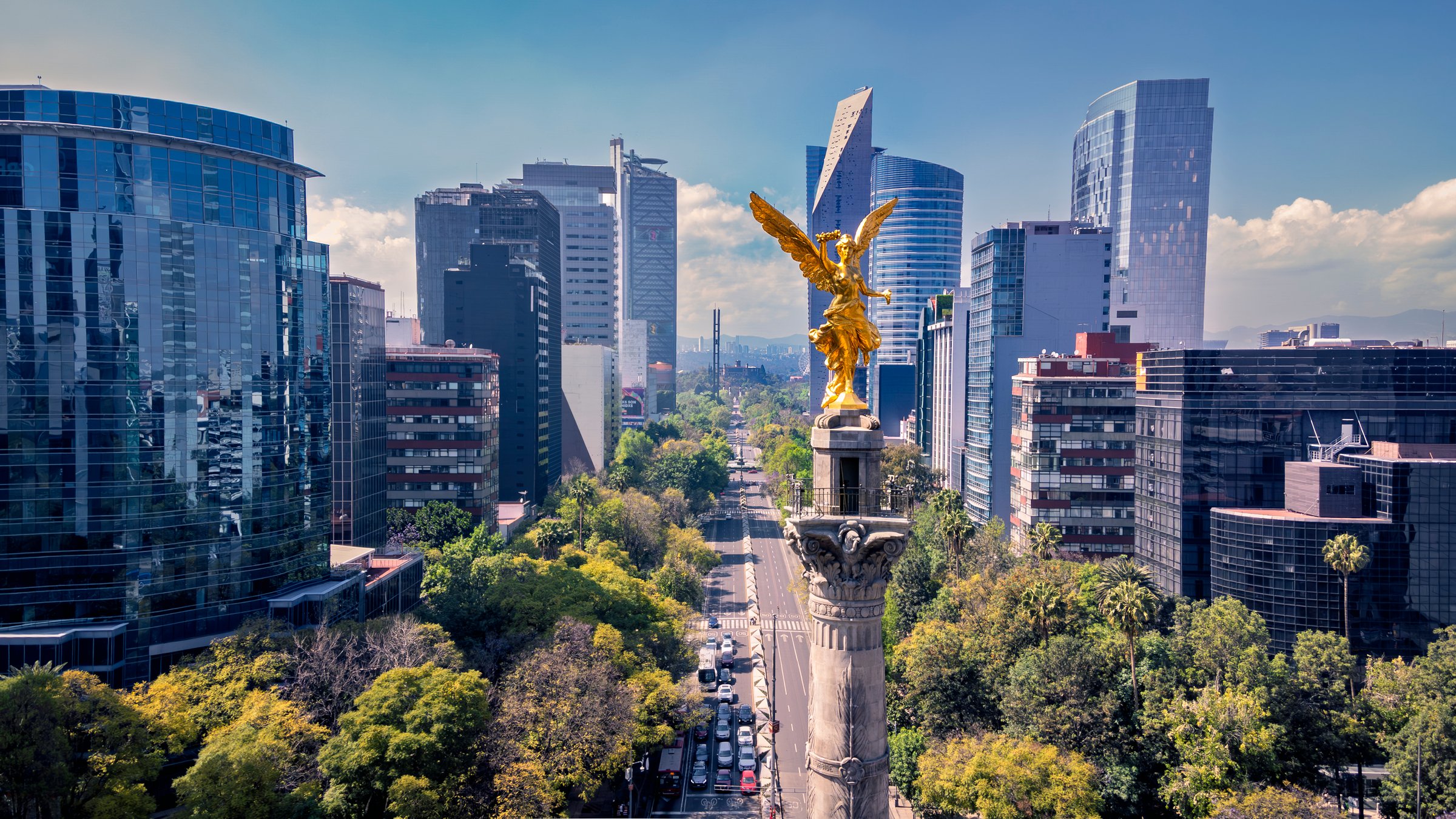The golden Angel of Independence monument stands tall in Mexico City, surrounded by modern skyscrapers and lush trees. This iconic landmark symbolizes Mexico's history and resilience.