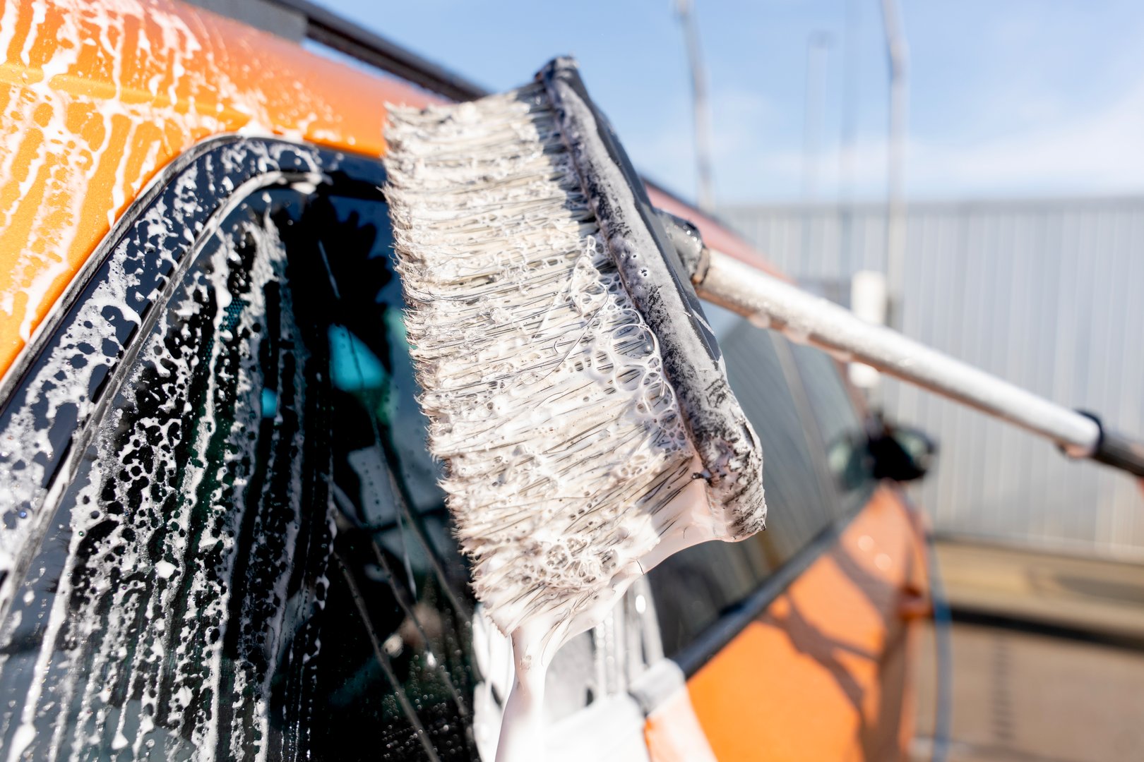 Water sprays across an orange car as brush bristles scrub away dirt