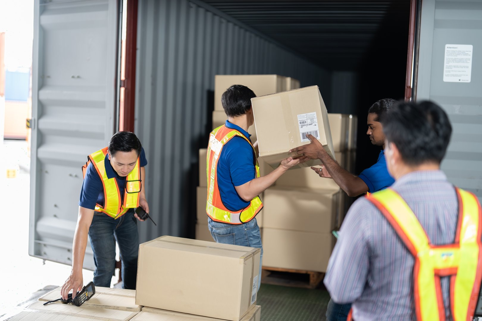4 men Warehouse worker open doors steel 40 feet container and help carry box one by one supervisor stand near by using paper clip checklist