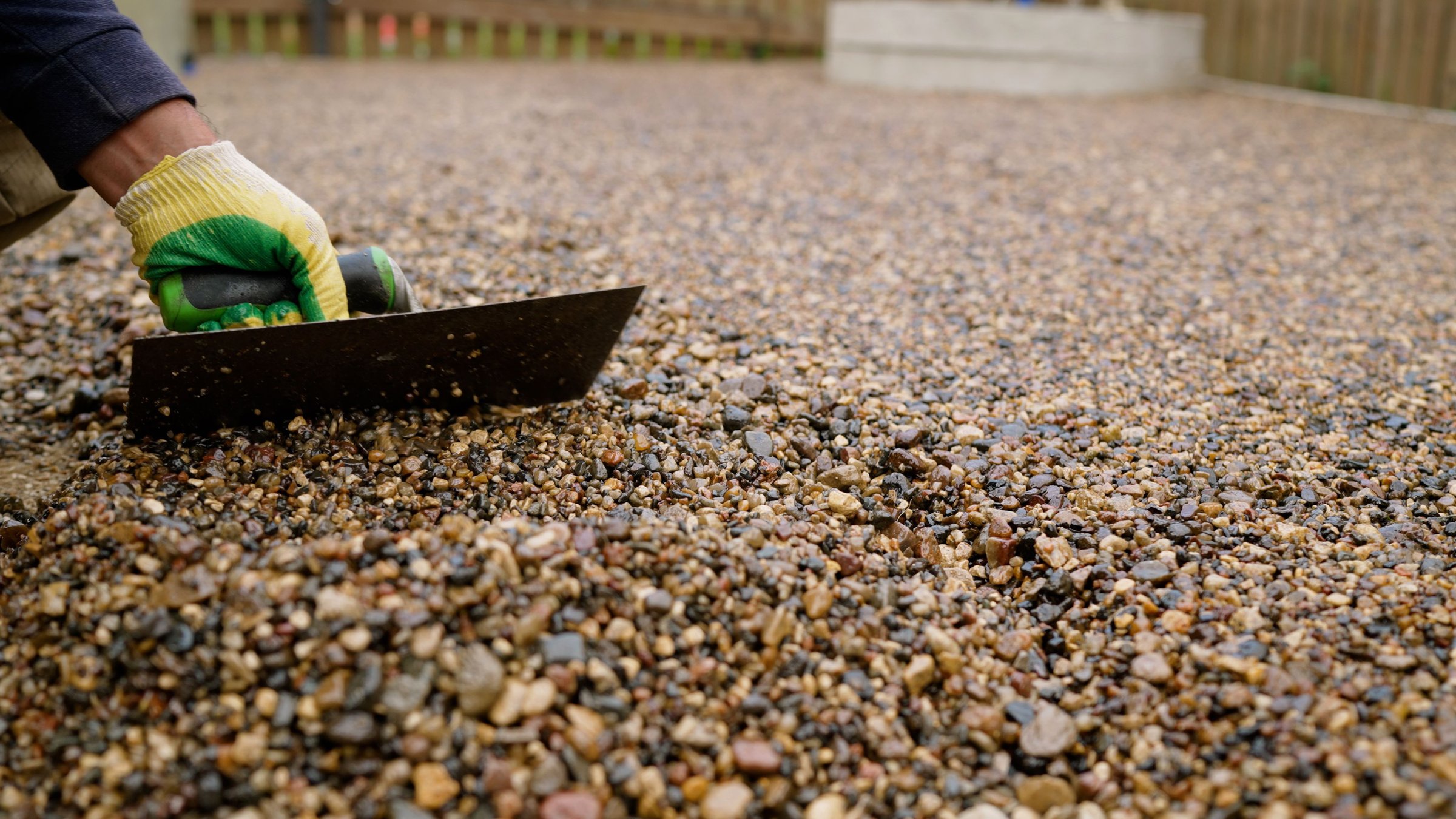 Construction worker carefully spreading gravel across concrete floor, leveling surface using professional trowel with precise manual technique