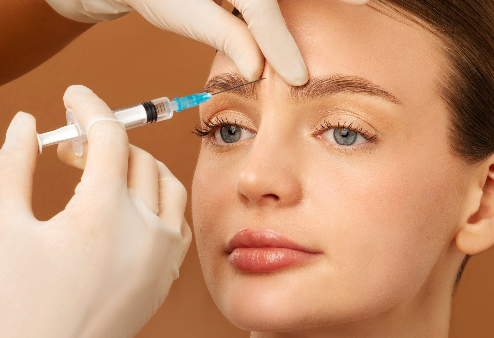 Young European lady receiving injection of anti-aging filler to forehead from professional cosmetologist in beauty salon, closeup shot