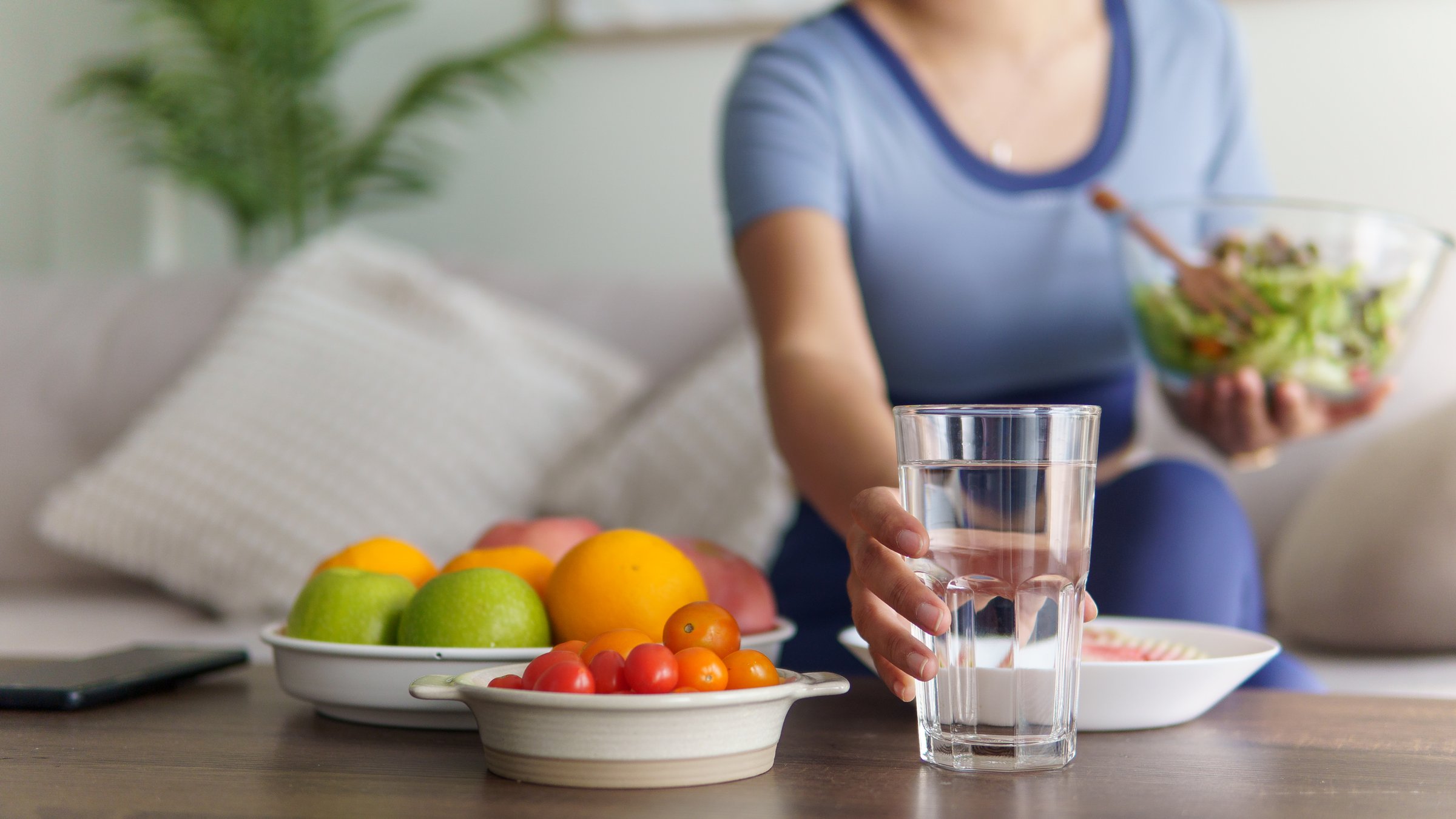 Young woman in activewear reaches for a glass of water while enjoying a healthy salad at home.