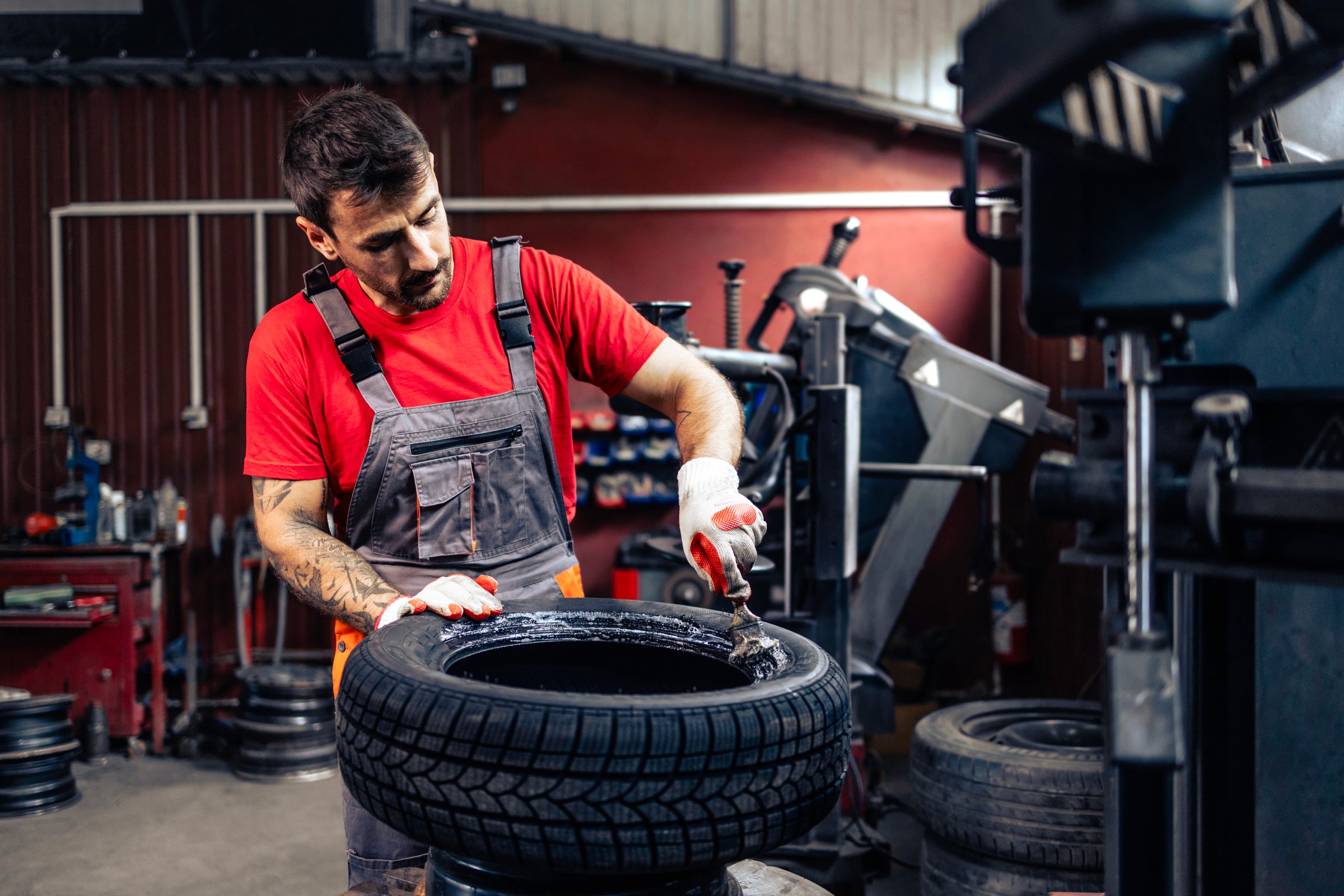 Tire repairman servicing car wheels inside workshop.