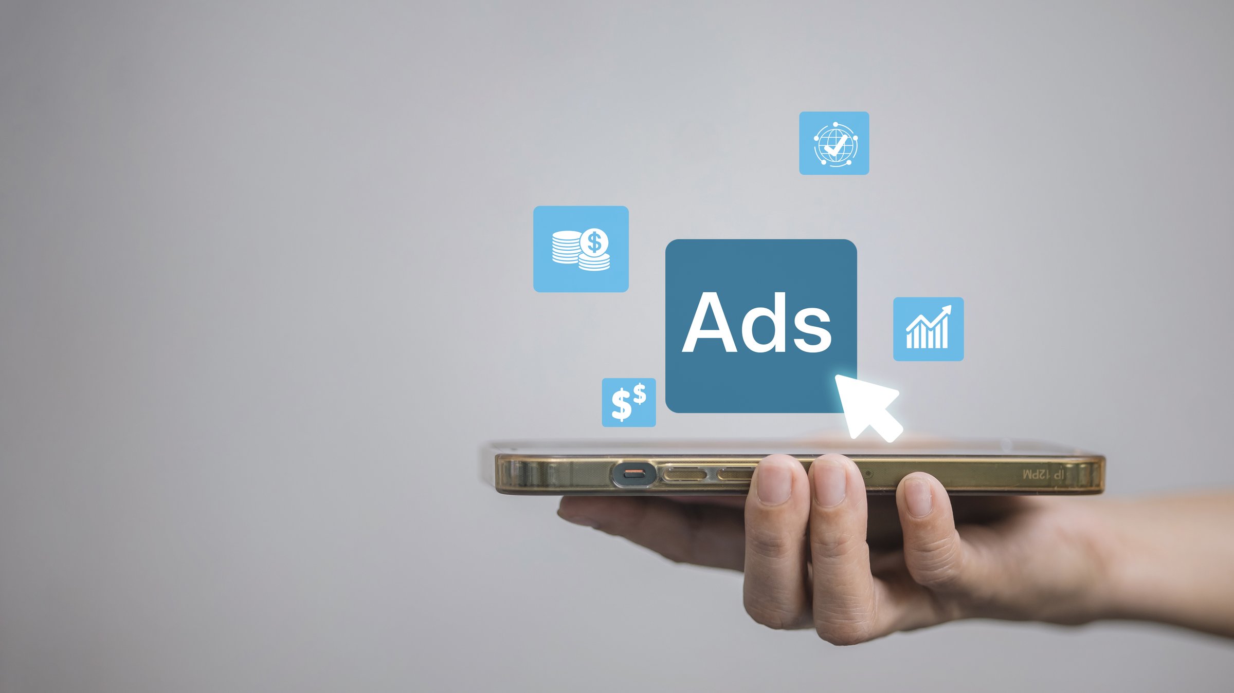 Hand holding smartphone with floating Ads button and finance icons, representing mobile advertising, PPC campaigns, social media promotion, ROI tracking, conversion and digital marketing growth.
