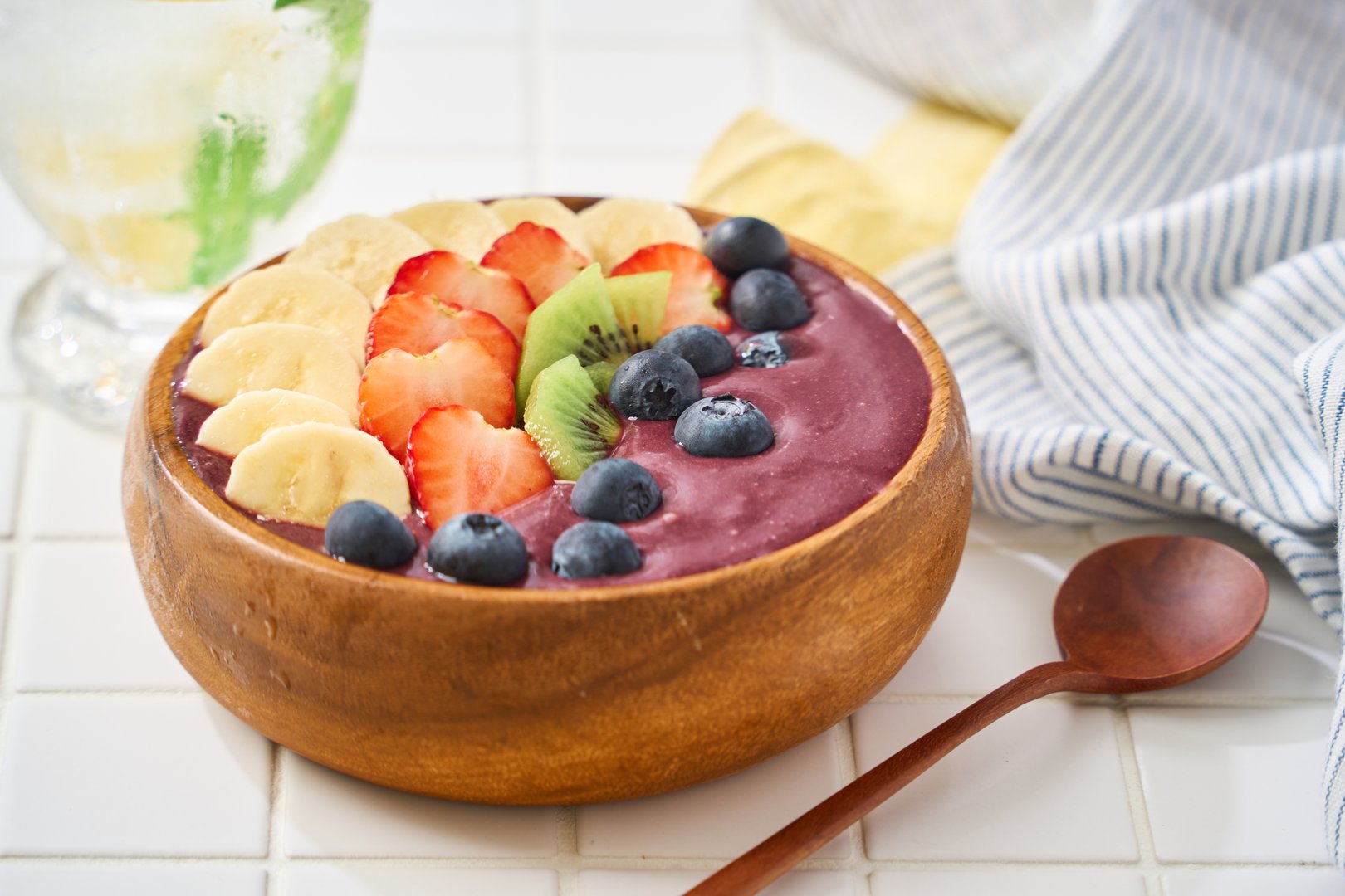 A healthy and colorful acai bowl topped with banana, strawberries, kiwi, and blueberries. Served in a wooden bowl with a bright and refreshing atmosphere, ideal for breakfast or clean eating visuals.