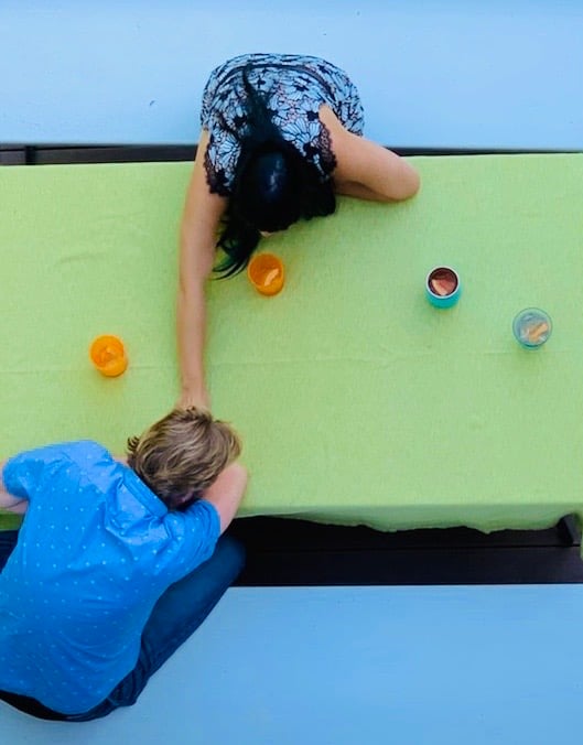Two people sit at a table with drinks on a light green tablecloth. One person is reaching across the table.