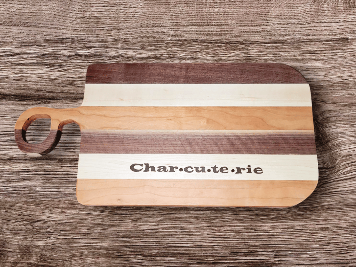 Wooden charcuterie board with striped design and "Charcuterie" text, placed on a wooden surface.
