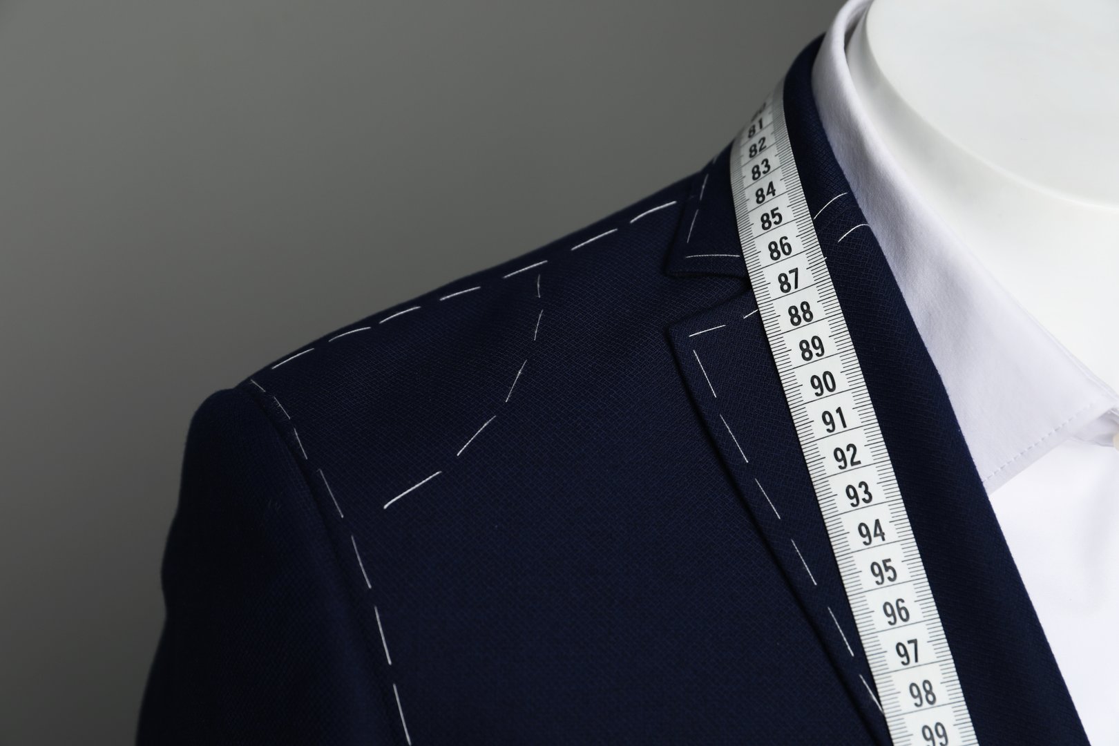 Semi-ready jacket with tailor's measuring tape and white shirt on mannequin against grey background, closeup