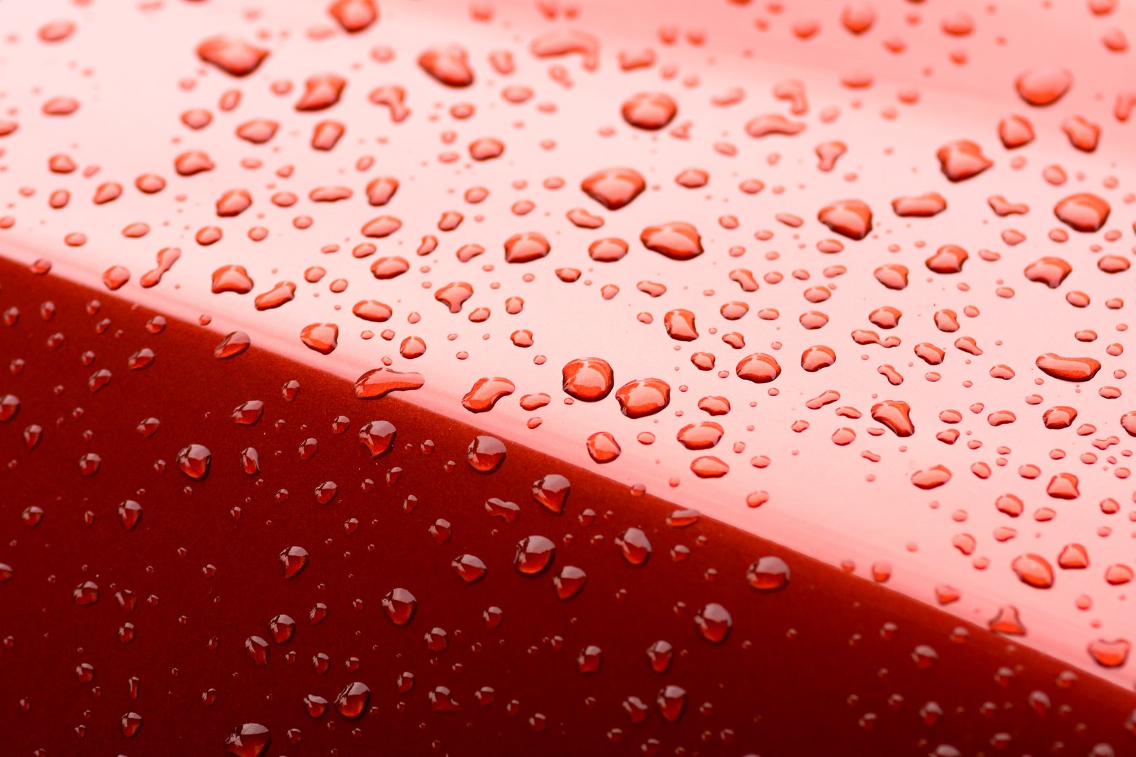 Close-up of red glossy surface with water droplets, showing detail of wet texture and fresh, clean appearance. Ideal for themes of automotive, moisture, and surface texture.