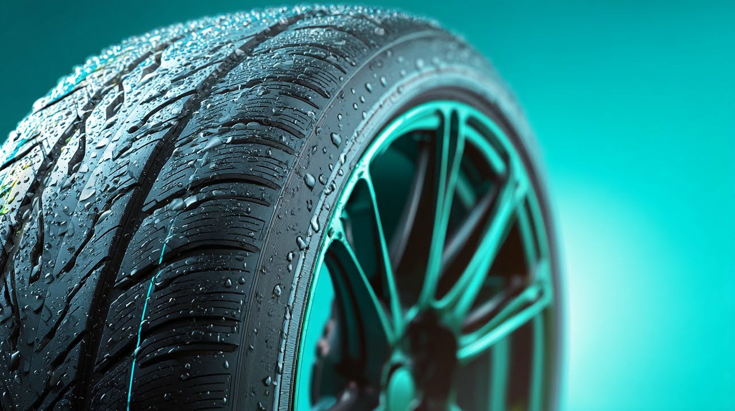 Close-up of a wet car tire with water droplets on a turquoise background, showcasing tread detail.