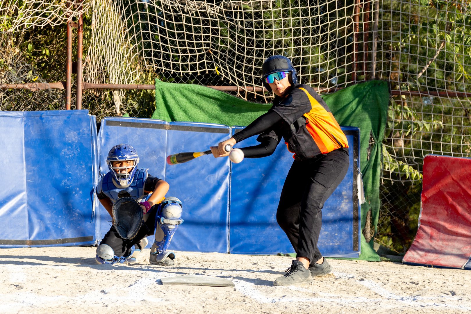Youth batter hitting a softball with focus as the catcher prepares to receive the ball behind home plate in an action game