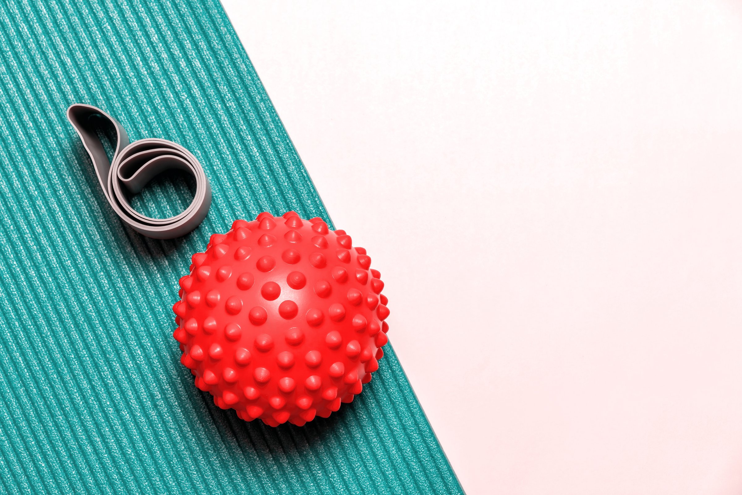 Red spiky ball and a grey resistance band lie on a blue yoga mat. This image is perfect for representing a home workout or fitness concept