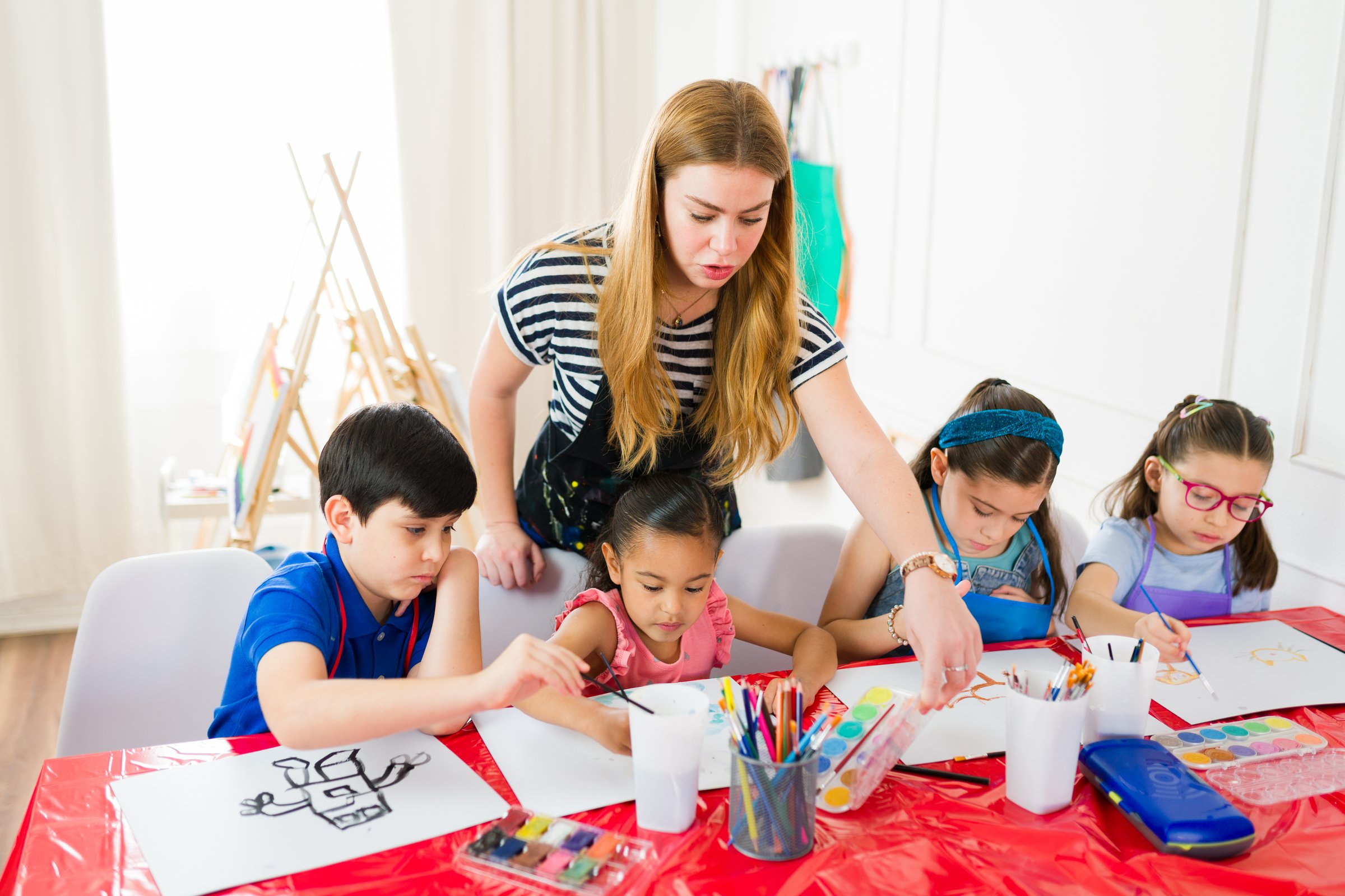 Art teacher assisting a group of diverse elementary school students with watercolor painting during art class