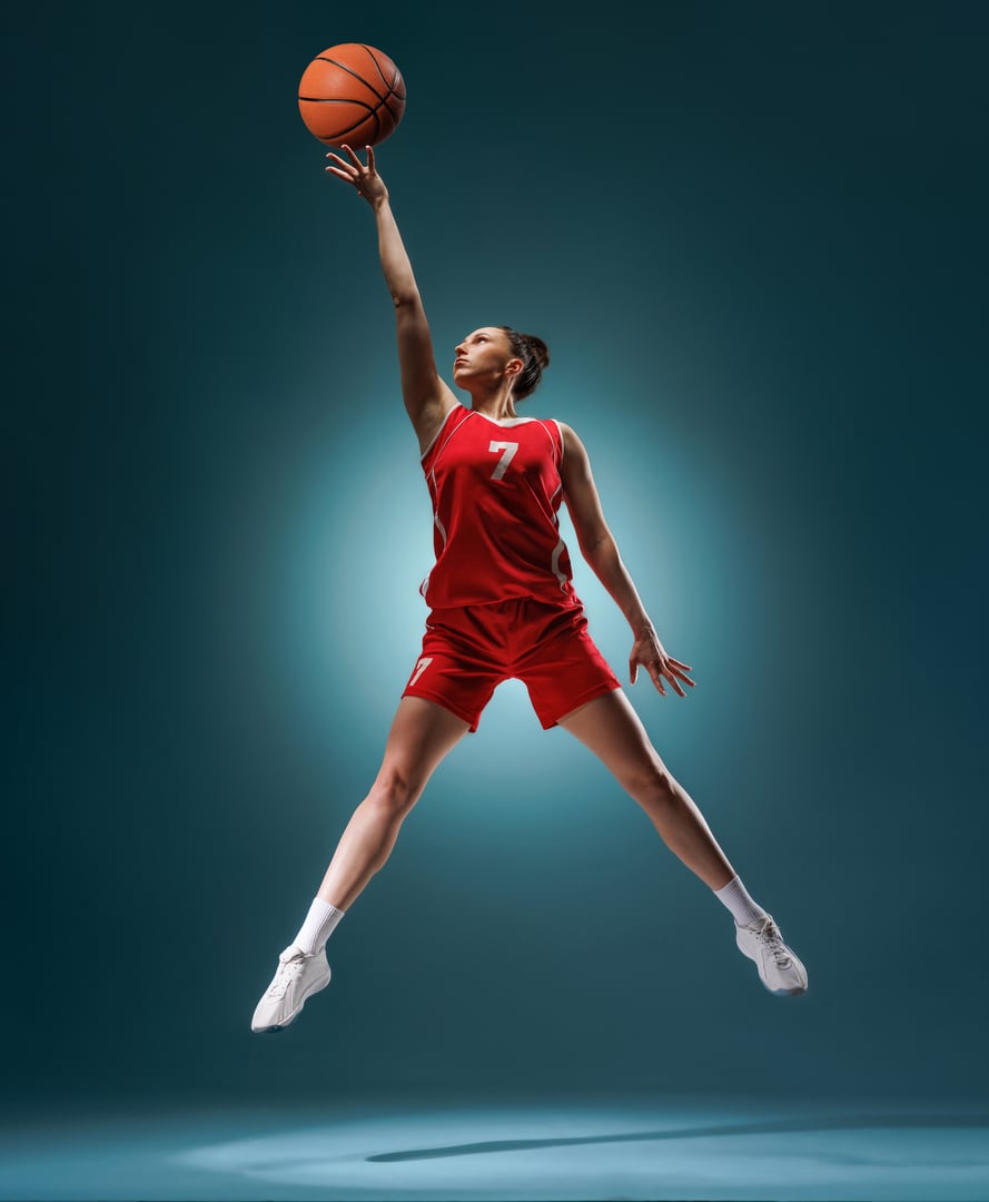 Young woman in red basketball uniform jumps to score, isolated against a dramatic blue background. Athletic, dynamic, and competitive.