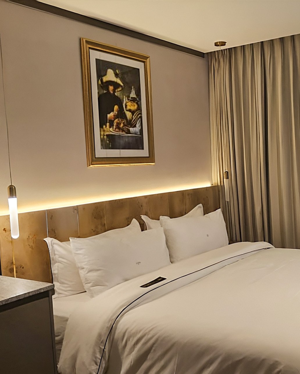 A man in a cap and apron posing in front of an art painting featuring blue and white figures with a monkey