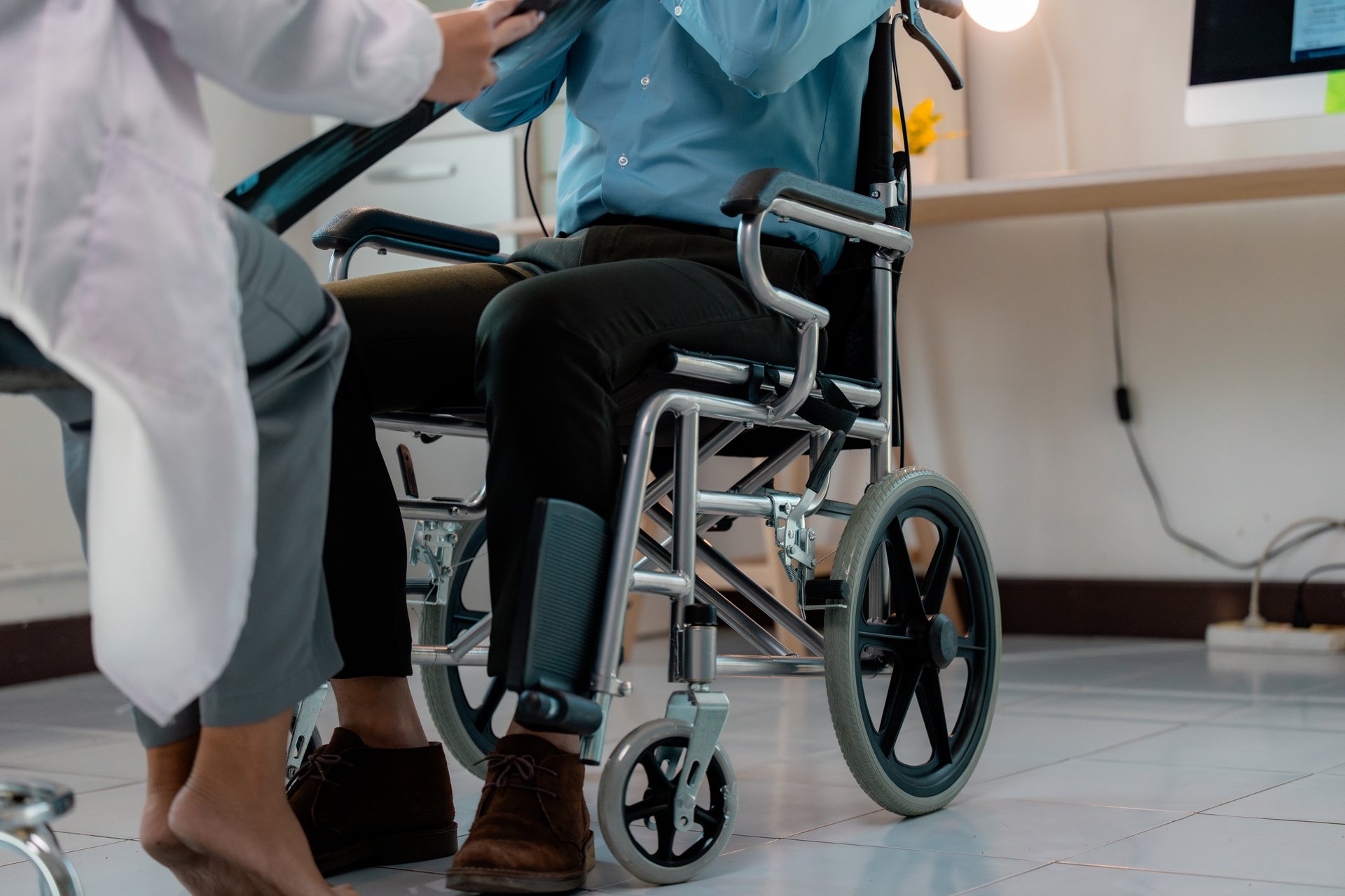 Doctor discussing an x-ray with a patient in a wheelchair during a medical examination in a hospital room, highlighting the importance of healthcare and accessibility